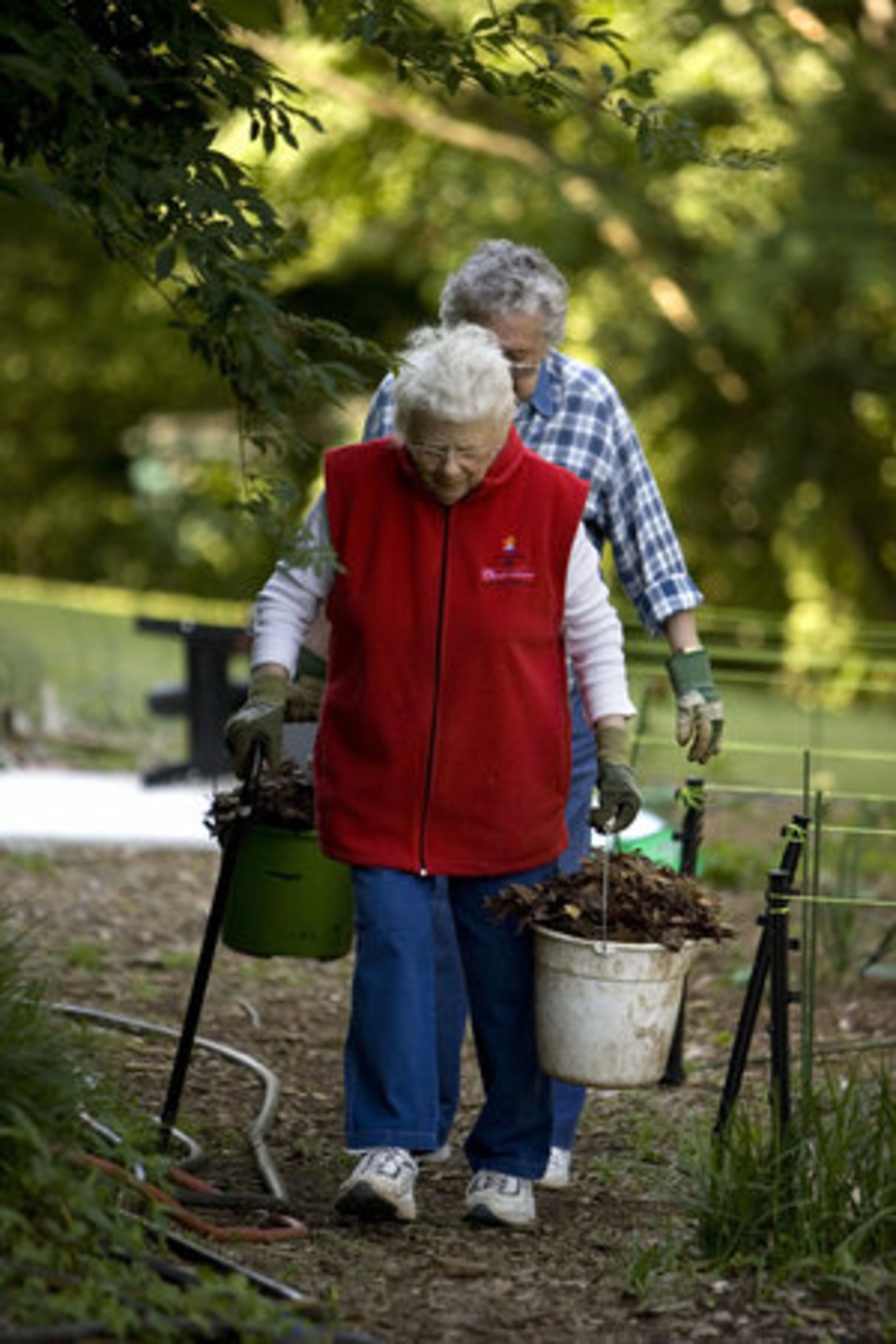 Carolyn Rhodes (front) and Ikey Howell carry buckets of mulch in the community garden at Decatur Christian Towers. A good gardener knows that mulching inhibits weeds and conserves water.