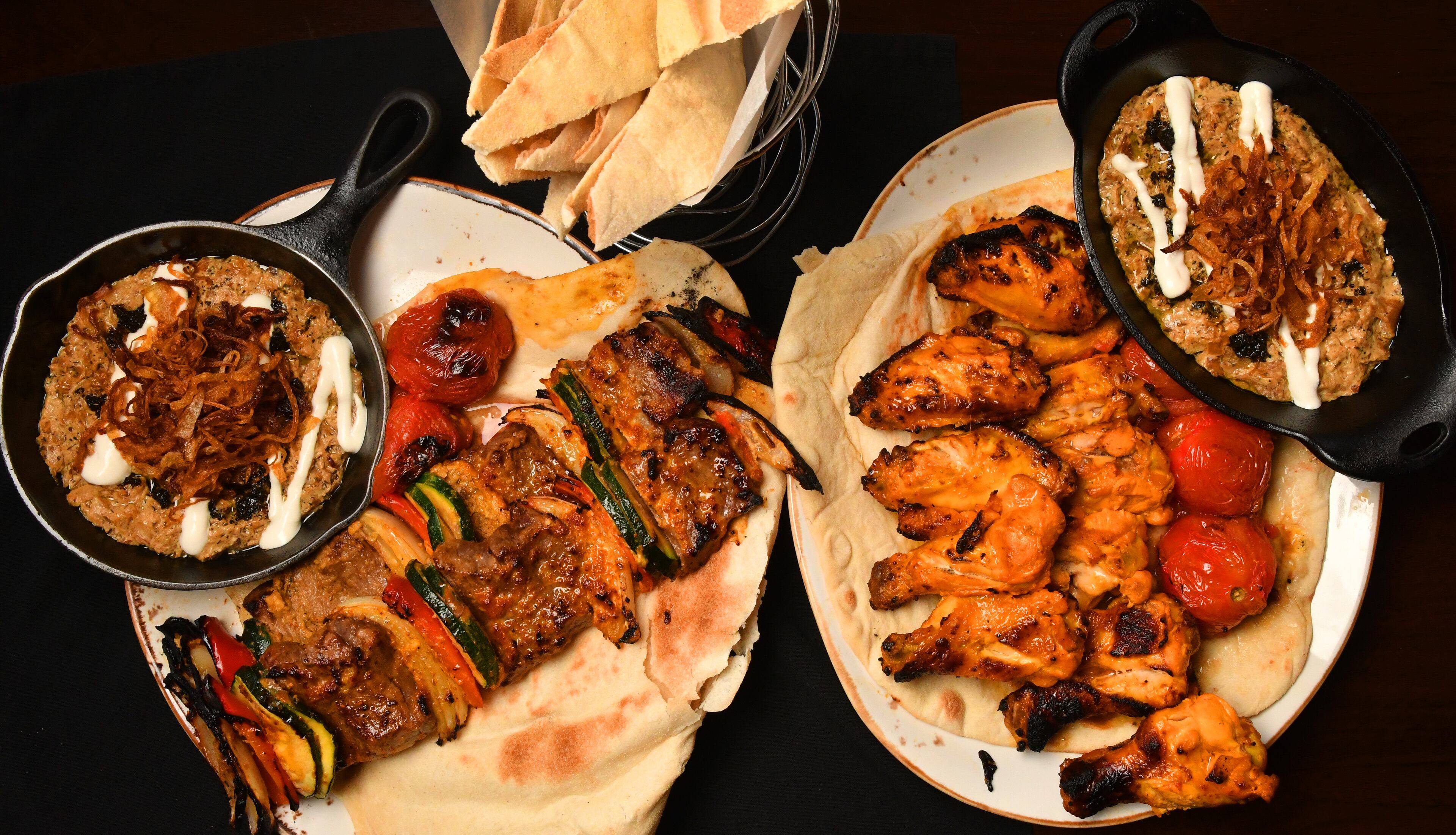Kashk Bademjoon (eggplant spread with crispy mint and fried onions), Beef Shish Kebabs, Zafron Wings, and a second dish of Kashk Bademjoon. Shown with bread in a basket at top. (Styling by Peter Teimori / Chris Hunt for the AJC)