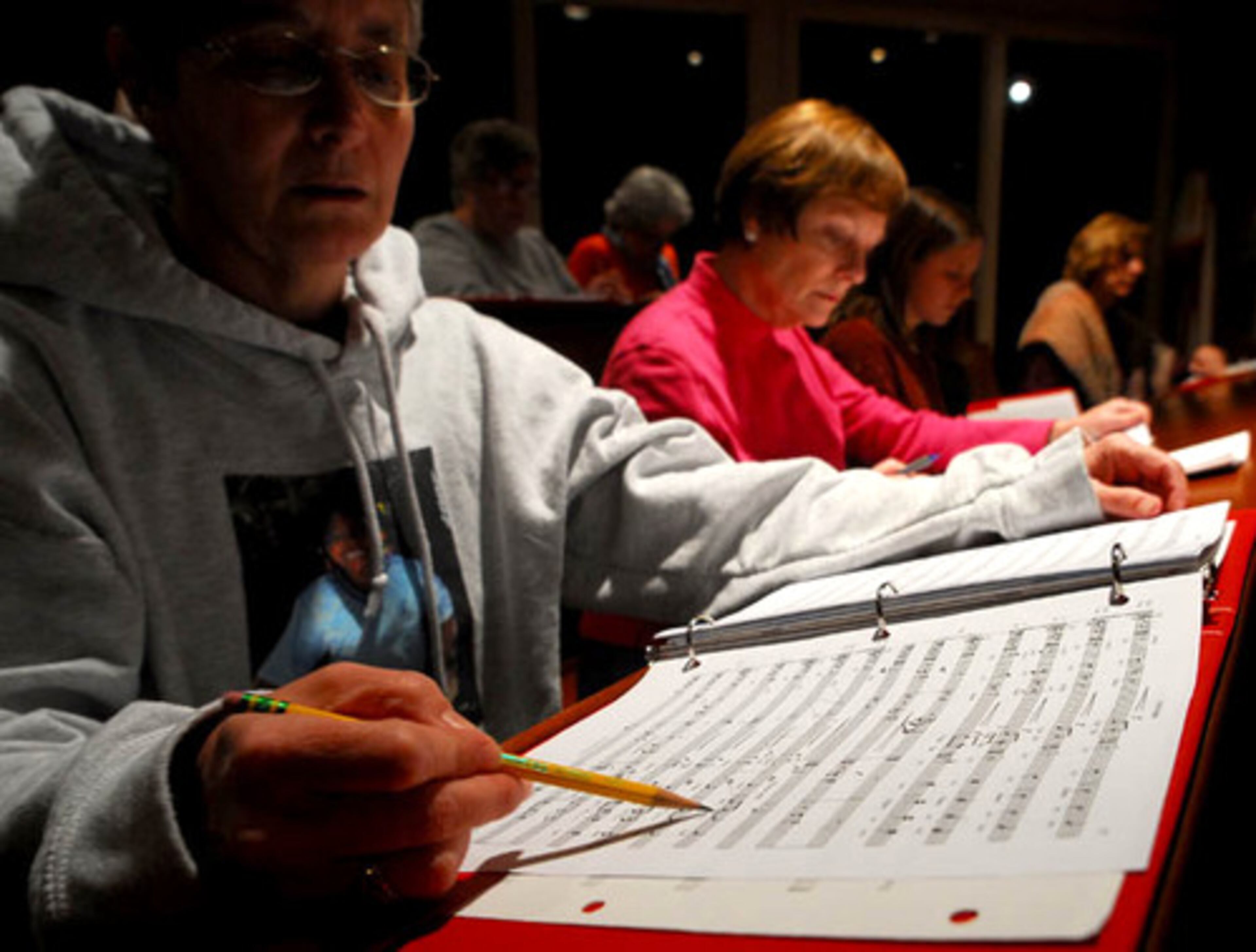 Mary Summerville, a soprano for St. Dunstan's Episcopal church choir in Sandy Springs, follows along as Choirmaster Stephen L. Furches outlines a certain area in the commissioned piece "In the Garden by composer, James Stevenson, during practice in the chapel of the church.