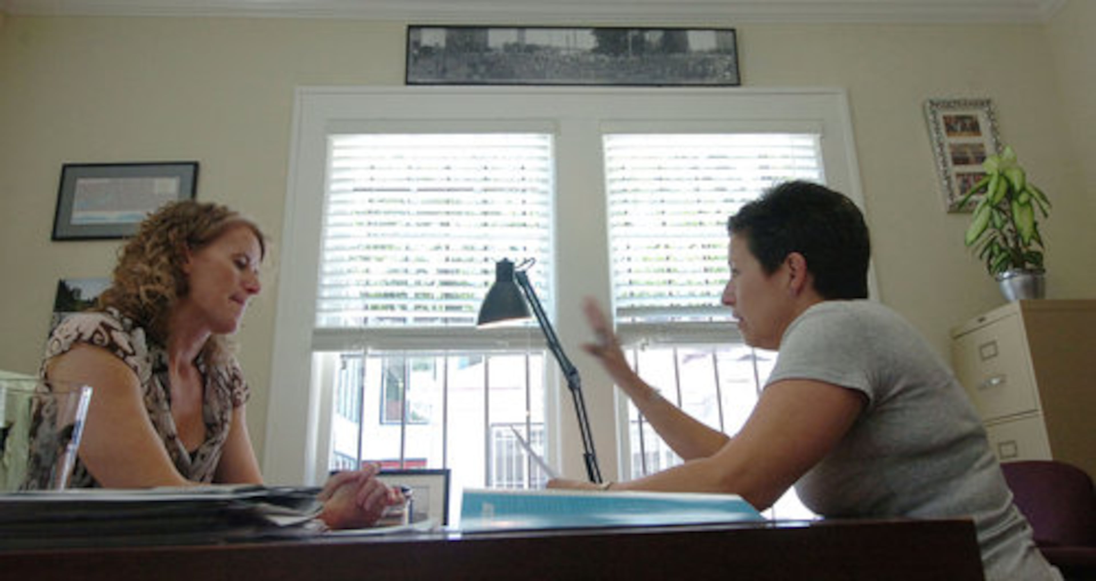 Russell (left) goes over some track club business with Janet Monk, one of her staff members. On the wall above them is a black and white panoramic photograph taken of the Peachtree Road Race in the early 1990's.
