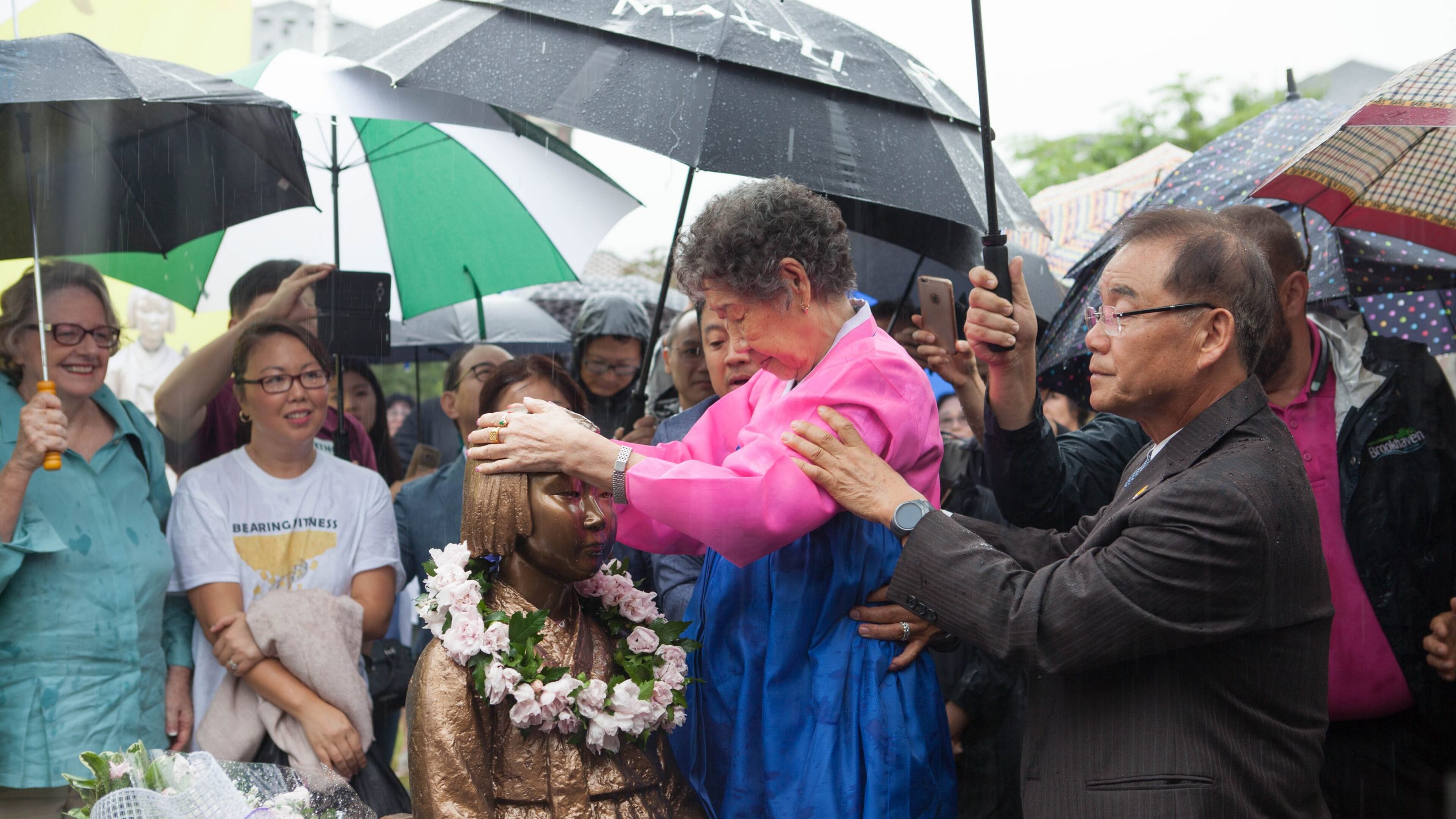 In a photo from the June 30 unveiling of the Comfort Women memorial statue in Brookhaven, Il-Chul Kang, 89, a Korean survivor of the atrocity, places her hands on the head of the bronze figure. Photo: David Kwon/The Korea Daily