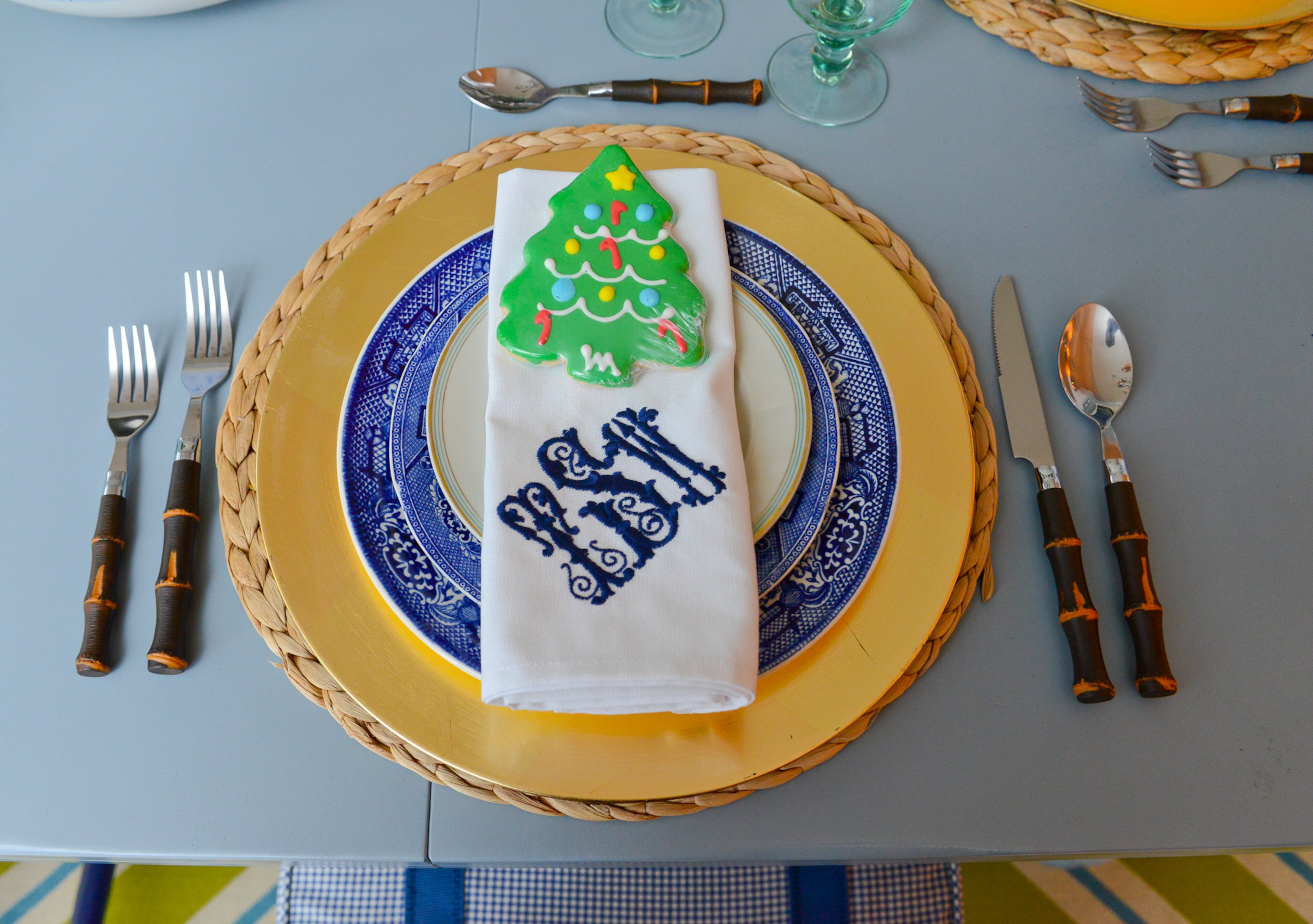 A Christmas tree cookie is a sweet accent to the blue and gold place settings for a holiday meal. The napkins are monogrammed with homeowner Travis Snyder's initials.