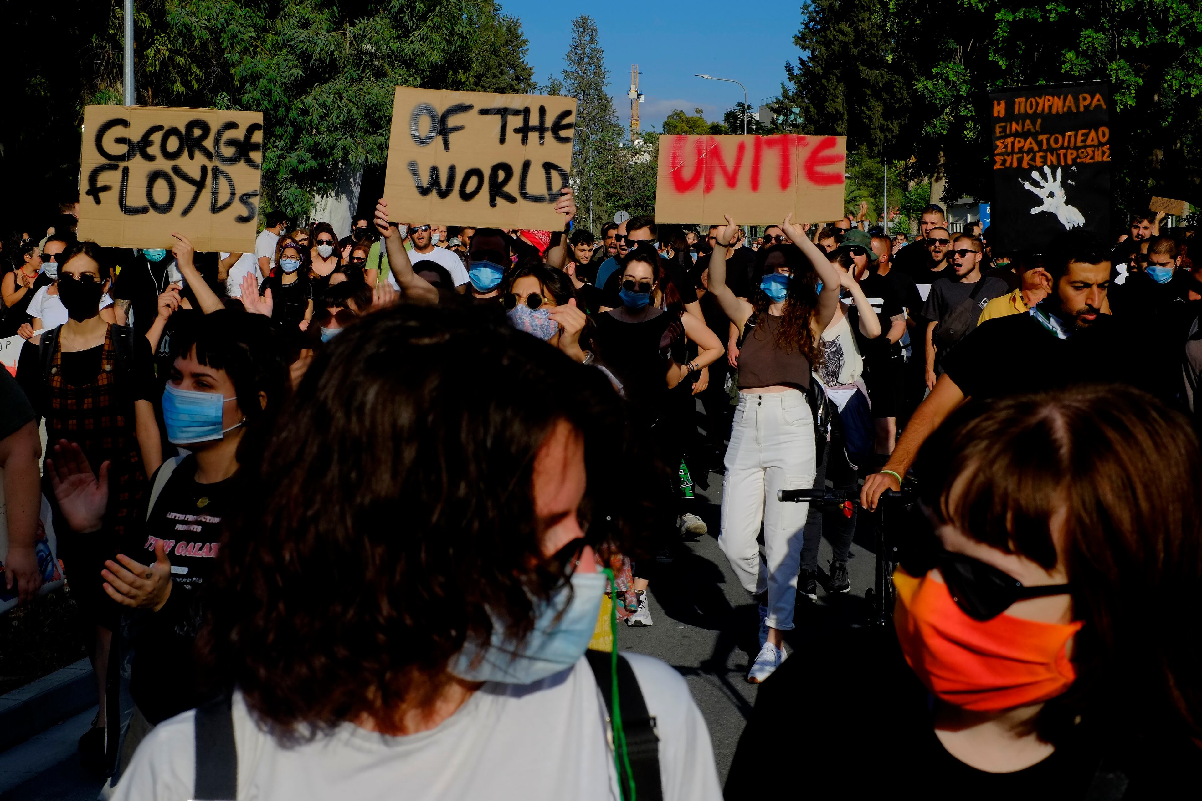 Three protesters, in the background, marching in support of detained migrants in Cyprus hold up placards to demonstrate their solidarity with African-American man George Floyd who died while pleading for his life, in capital of Nicosia, Cyprus, on Sunday, May 31, 2020. Floyd's death, the latest in a series of deaths of black men and women at the hands of police in America, triggered five days of civil unrest in the United States and marches in several European countries. (AP Photo/Petros Karadjias)