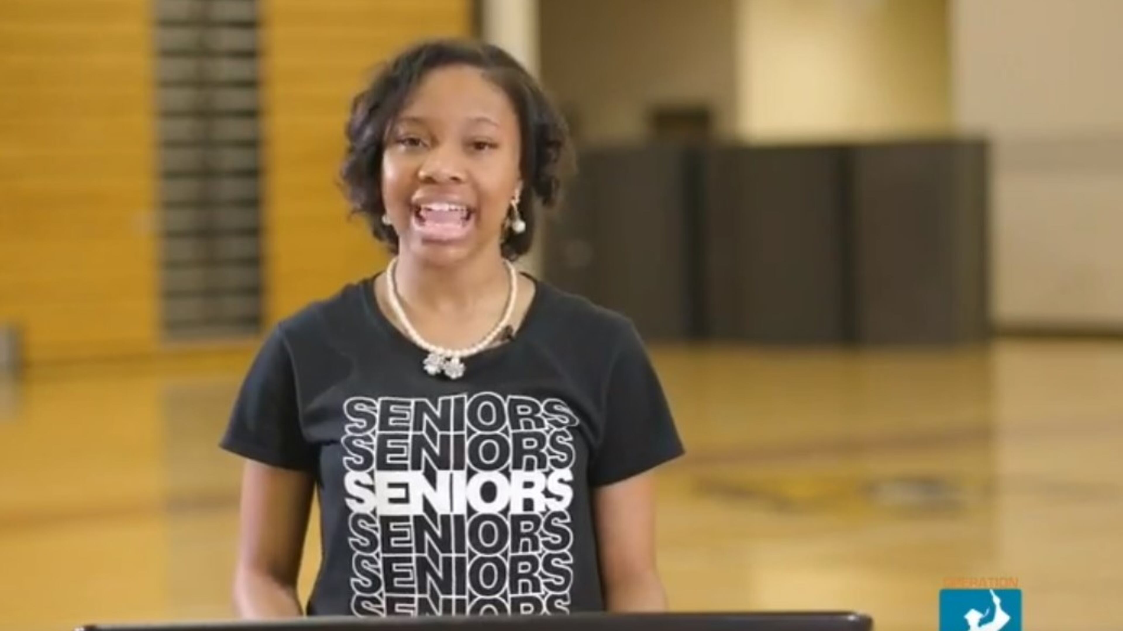 A screenshot of Lauren Hester, valedictorian of Coretta Scott King Young Women's Leadership Academy in Atlanta, as she gives a speech in an empty gym during a video celebrating graduation.