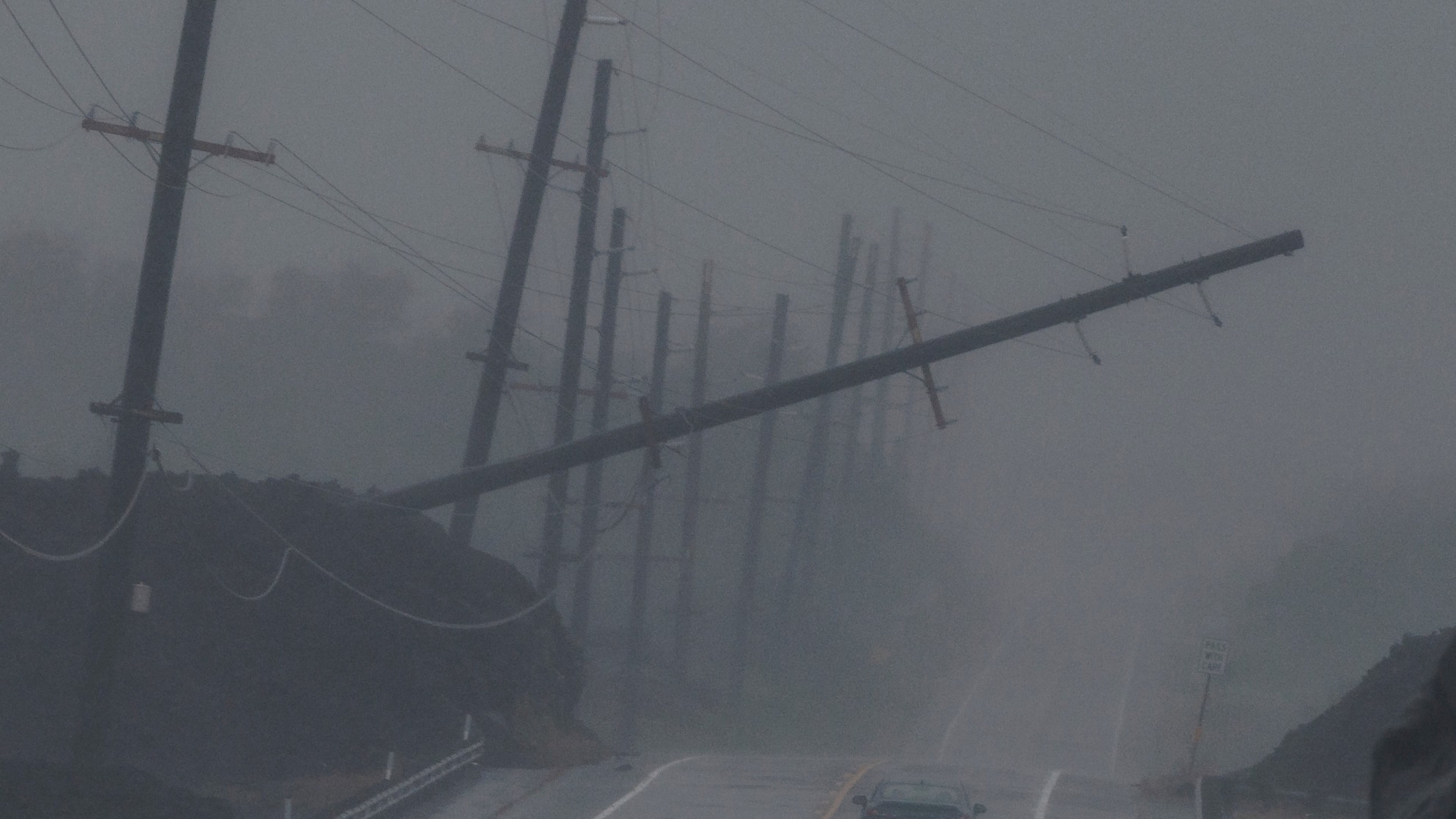 A vehicle drives near a downed utility pole dangling above Mamalahoa Highway during Hurricane Lala near Ocean View, Hawaii, Saturday, Aug. 15, 2026. (Stephen Lam/San Francisco Chronicle via AP)