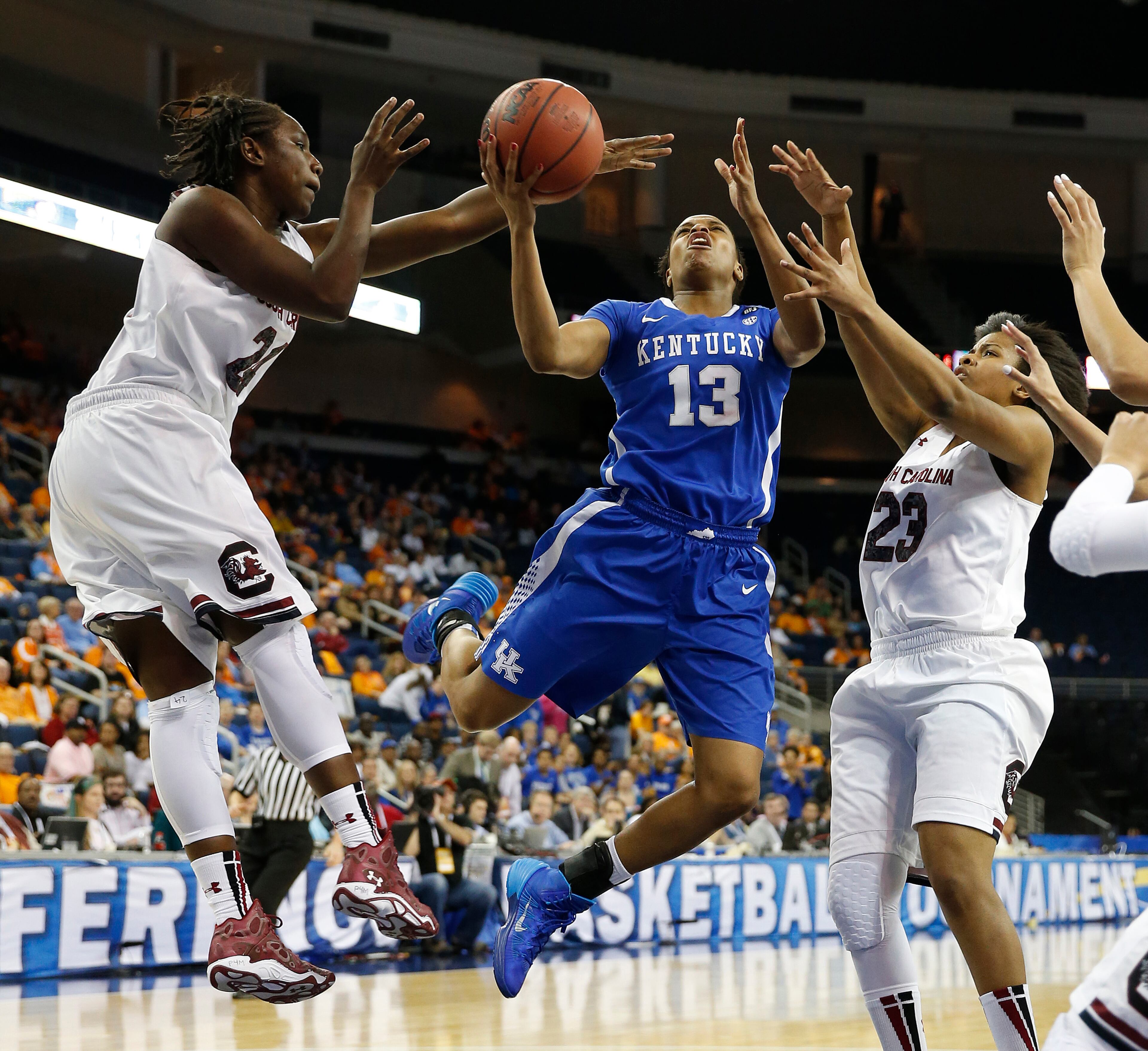 Kentucky guard Bria Goss (13) is fouled as she drives between South Carolina forward Aleighsa Welch, left, and guard Tina Roy (23) during the first half of an NCAA college basketball game in the semifinals of the Southeastern Conference women's basketball tournament Saturday, March 8, 2014, in Duluth, Ga.