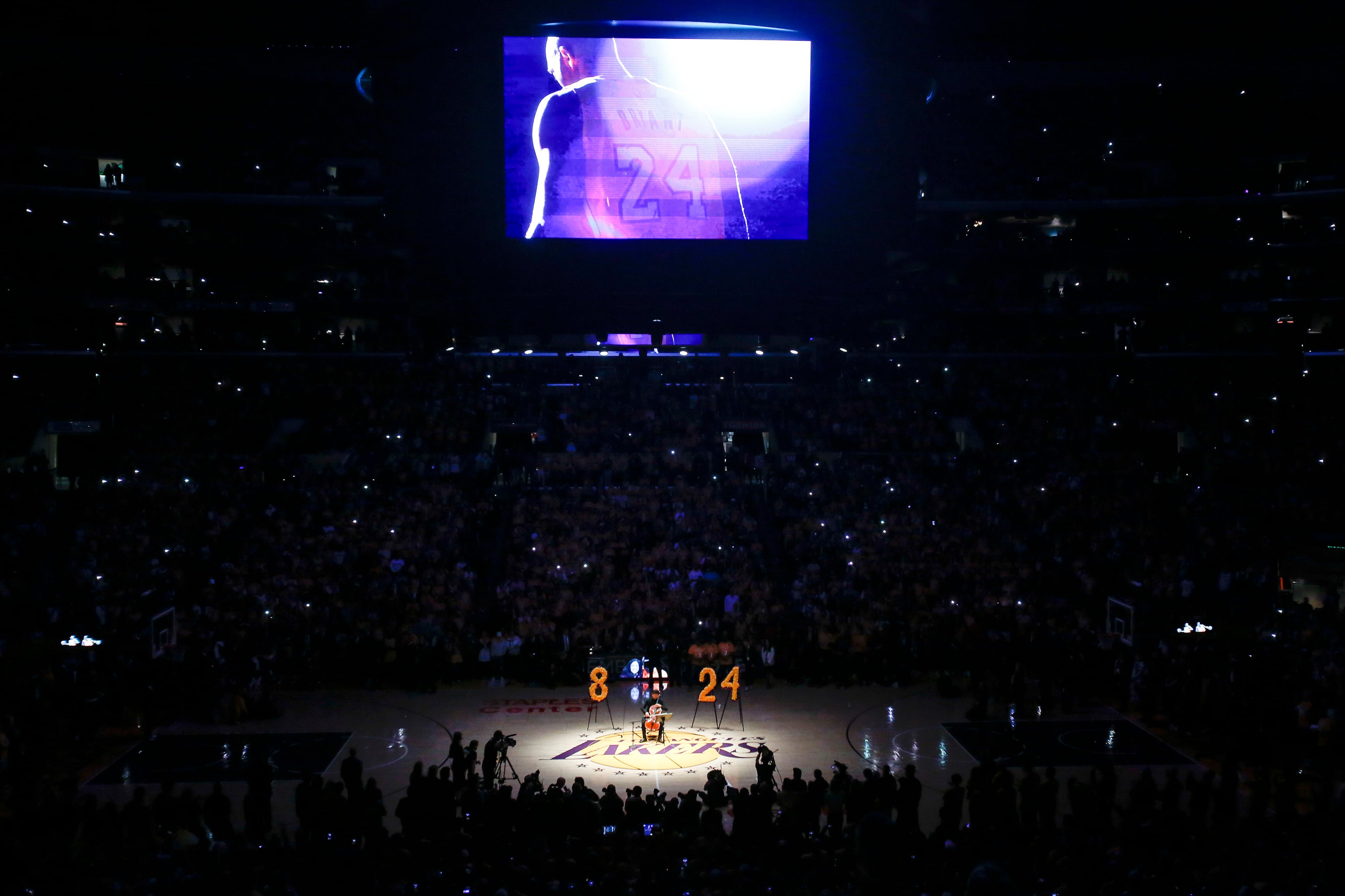 A video honoring late NBA player Kobe Bryant is shown on screen while cellist Ben Hong performs during a memorial prior to an NBA basketball game between the Los Angeles Lakers and the Portland Trail Blazers at Staples Center, Friday, Jan. 31, 2020, in Los Angeles. Bryant died in a helicopter crash Sunday. (AP Photo/Ringo H.W. Chiu)