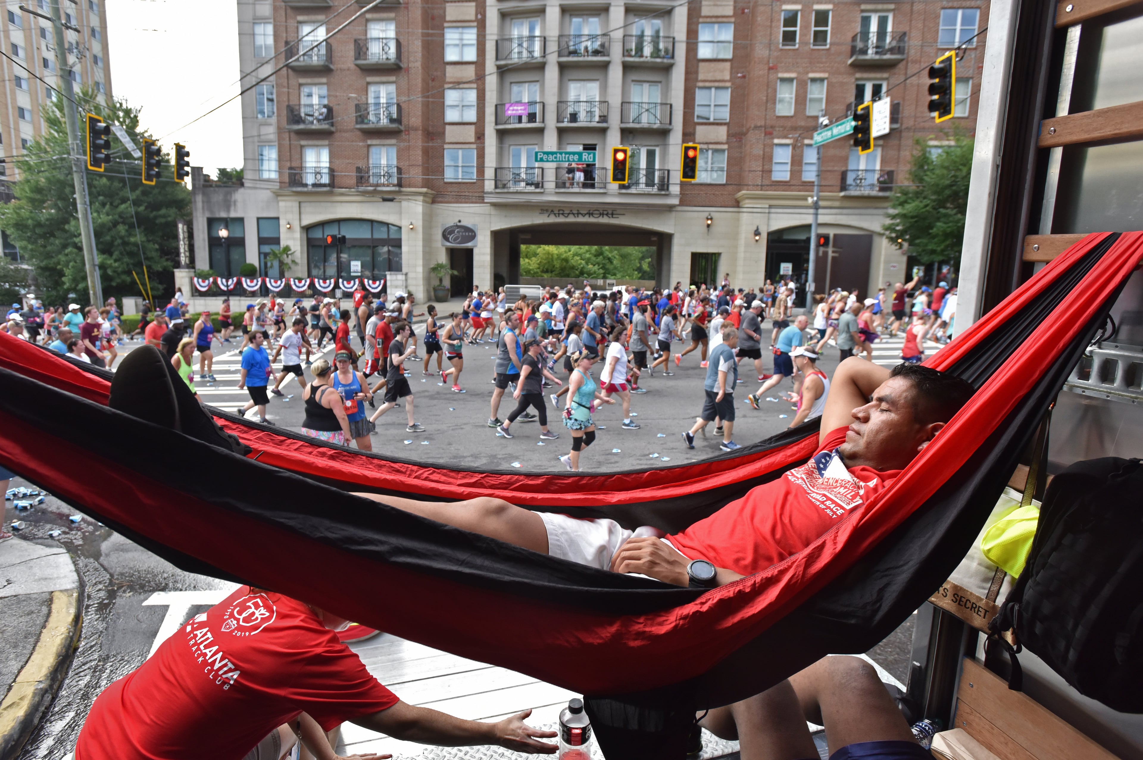A.J. Jensen (foreground), volunteer, takes a short nap as runners make their way down Peachtree Road during the 50th AJC Peachtree Road Race on Thursday, July 4, 2019. (Hyosub Shin / Hyosub.Shin@ajc.com)