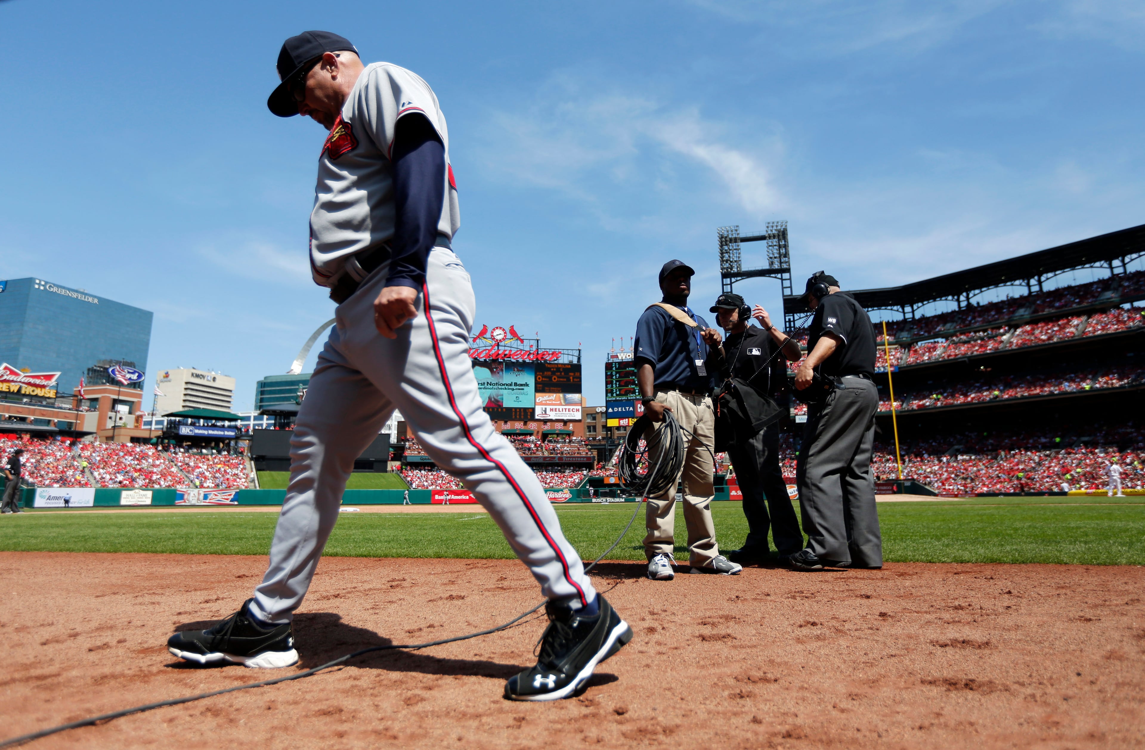 Atlanta Braves manager Fredi Gonzalez, left, steps over a cable as umpires Chris Guccione and Eric Cooper, right, review a call during the fifth inning of a baseball game Sunday, May 18, 2014, in St. Louis. (AP Photo/Jeff Roberson)