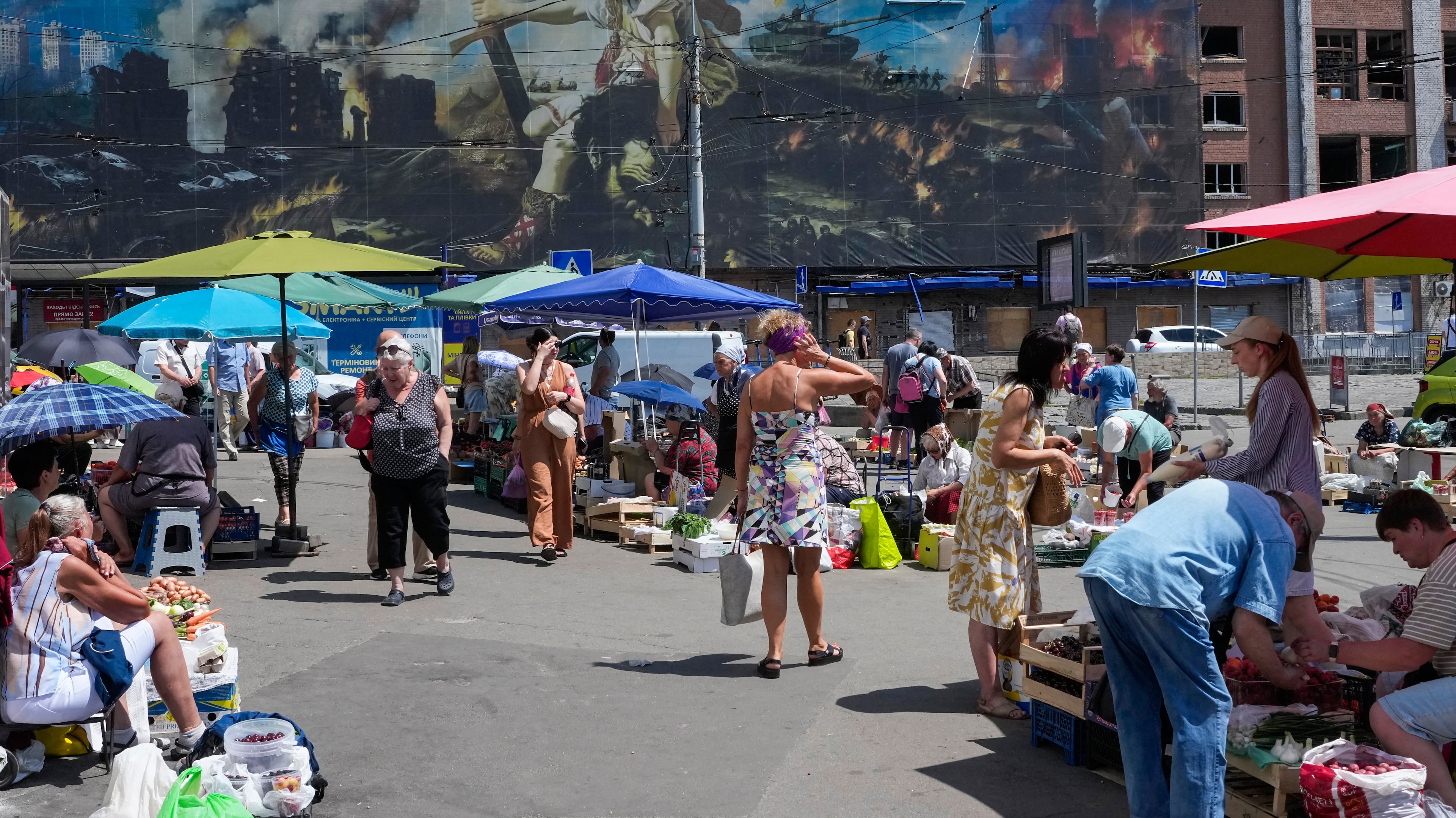 People buy food at an improvised outdoor market surrounded by damaged buildings covered with street artist paintings close to a big city marketplace that was ruined recently by Russian missiles in Kyiv, Ukraine, Monday, June 22, 2026. (AP Photo/Efrem Lukatsky)