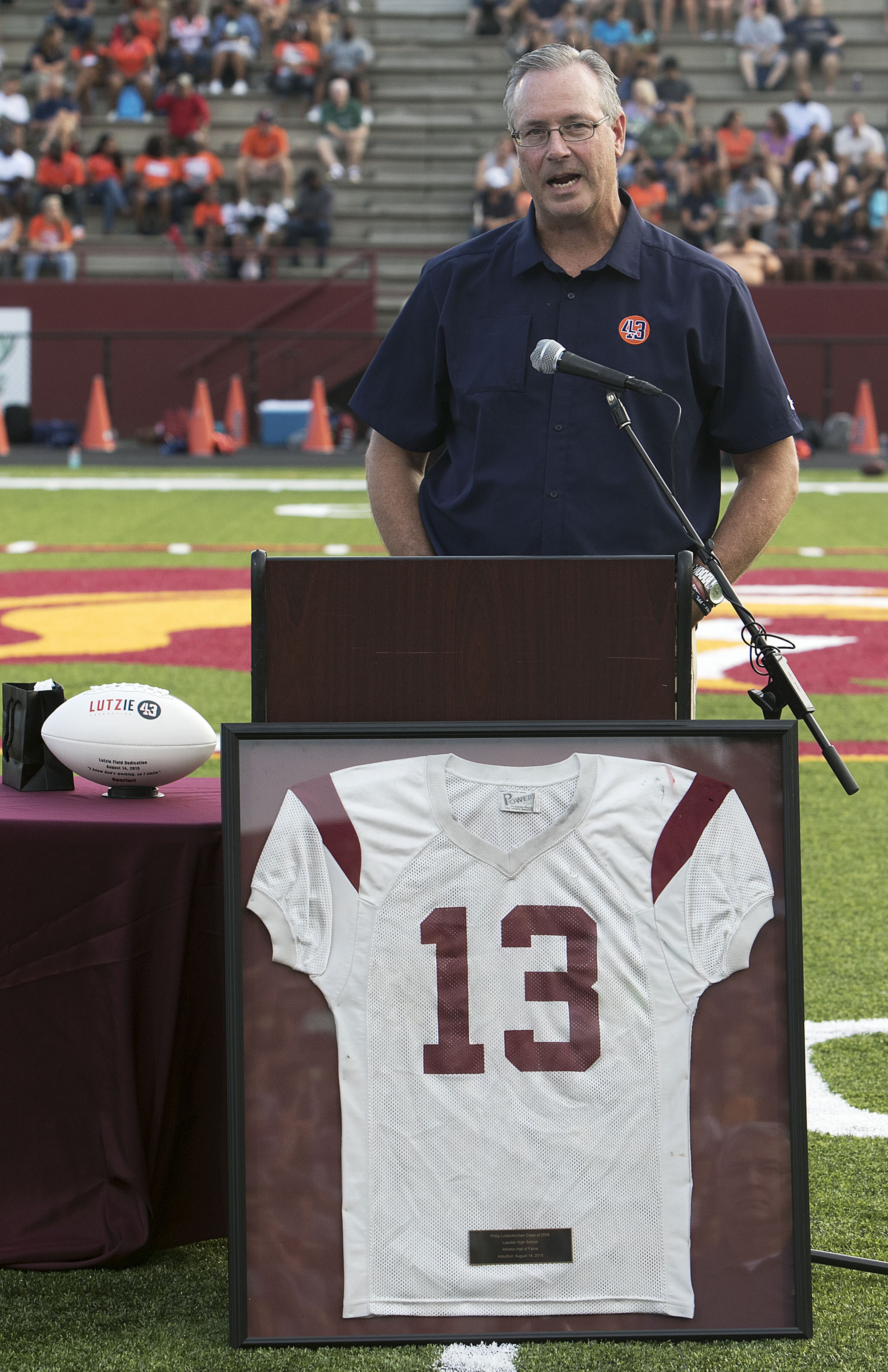 Mike Lutzenkirchen talks with his son Philip's # 13 jersey in front of him during a dedication of the newly resurfaced and newly named Lutzie Field at Lassiter High in Marietta on Friday August 14th, 2015. (Photo by Phil Skinner)
