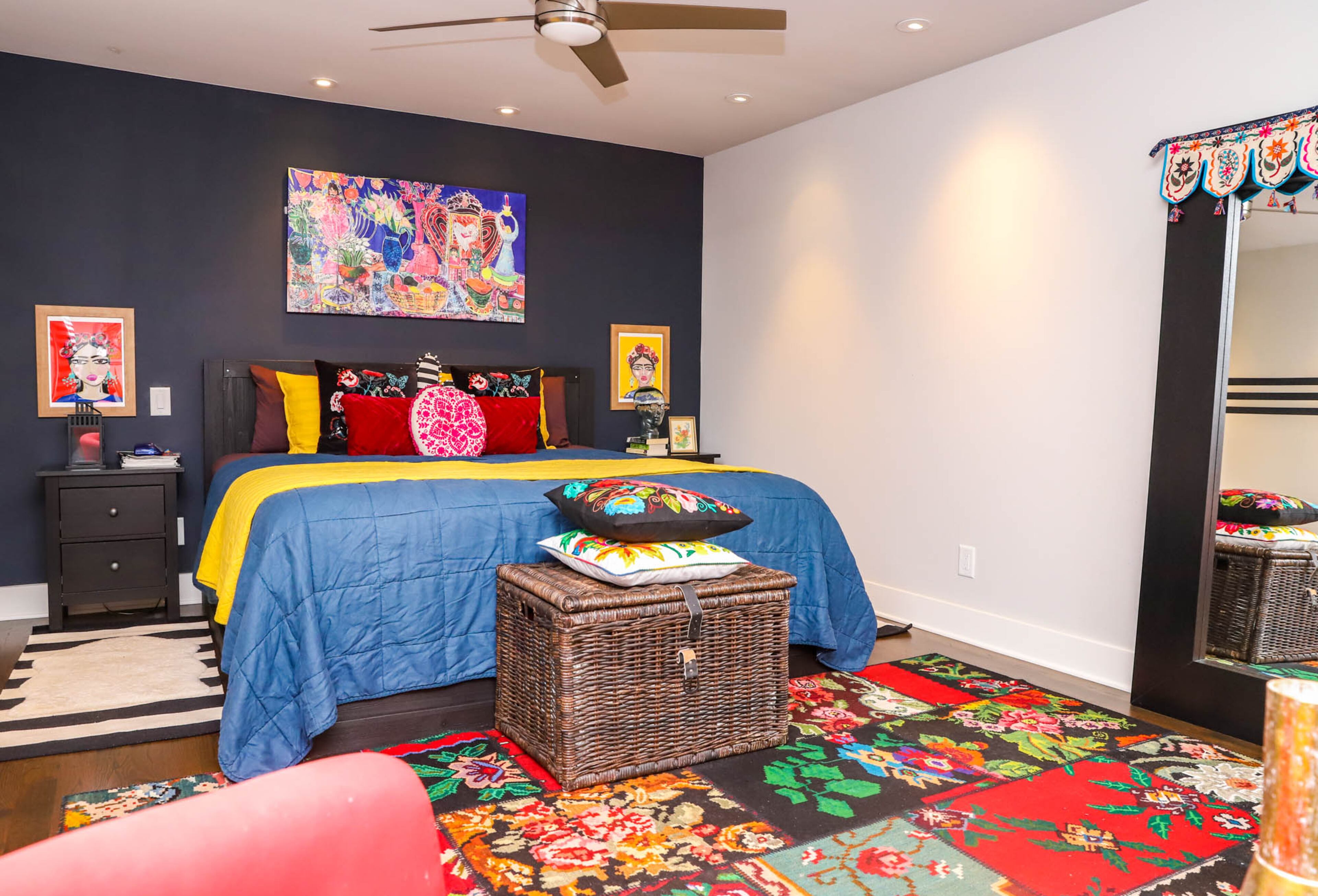 The master bedroom of Jeff and Paola Roder’s home has more muted colors than the common areas, with a color palette inspired by portraits of Frida Kahlo that hang on either side of the bed, both painted by Heather Felder, a Mexican and Norwegian artist. Over the bed hangs a vivid piece from Great Big Canvas, and the rug on the floor is a Turkish line from Ikea. Text by Shannon Dominy. Photo by Reynolds Rogers.