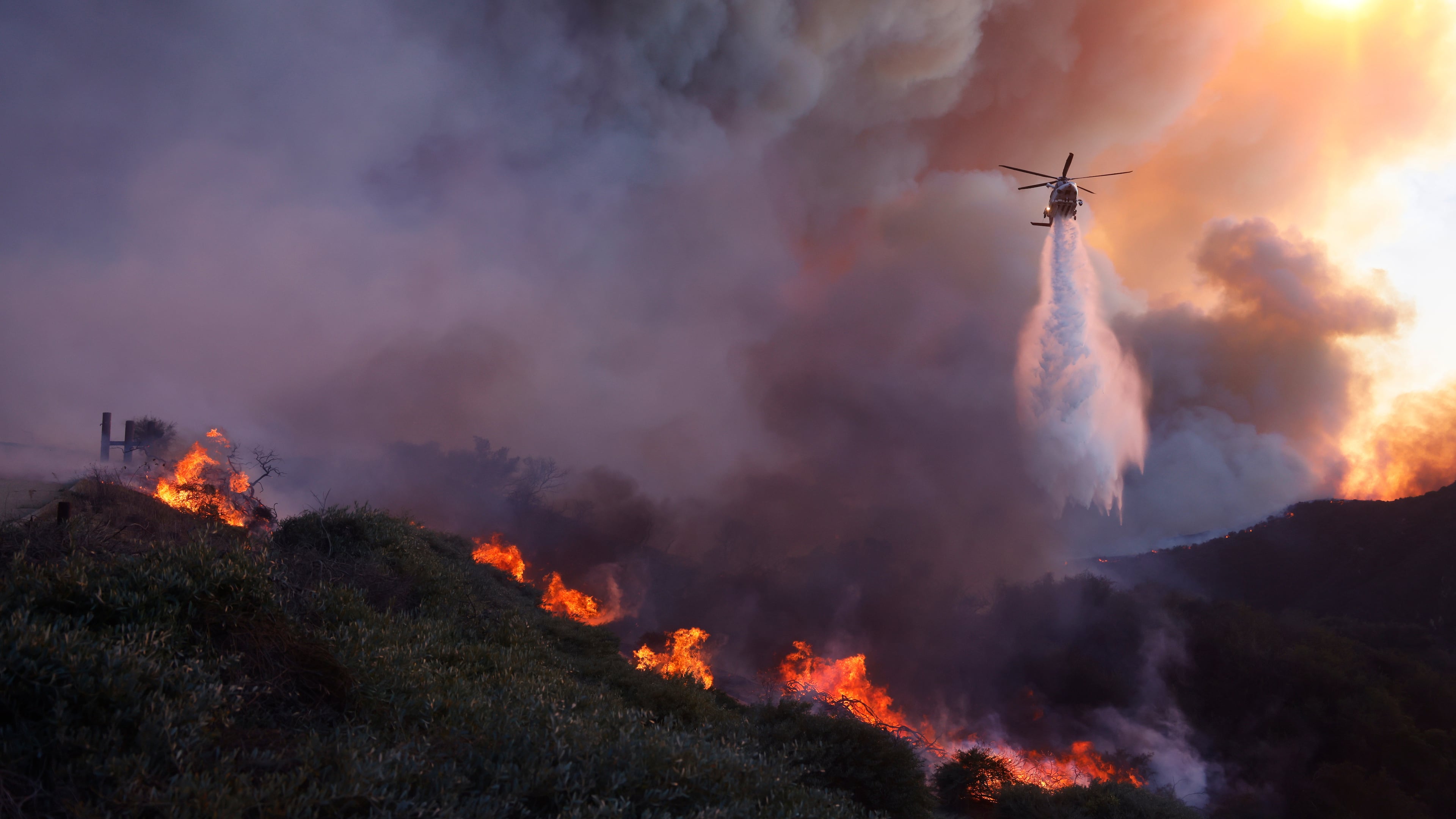 FILE - Water is dropped by helicopter on the advancing Palisades Fire in the Pacific Palisades neighborhood of Los Angeles, Jan. 7, 2025. (AP Photo/Etienne Laurent, File)