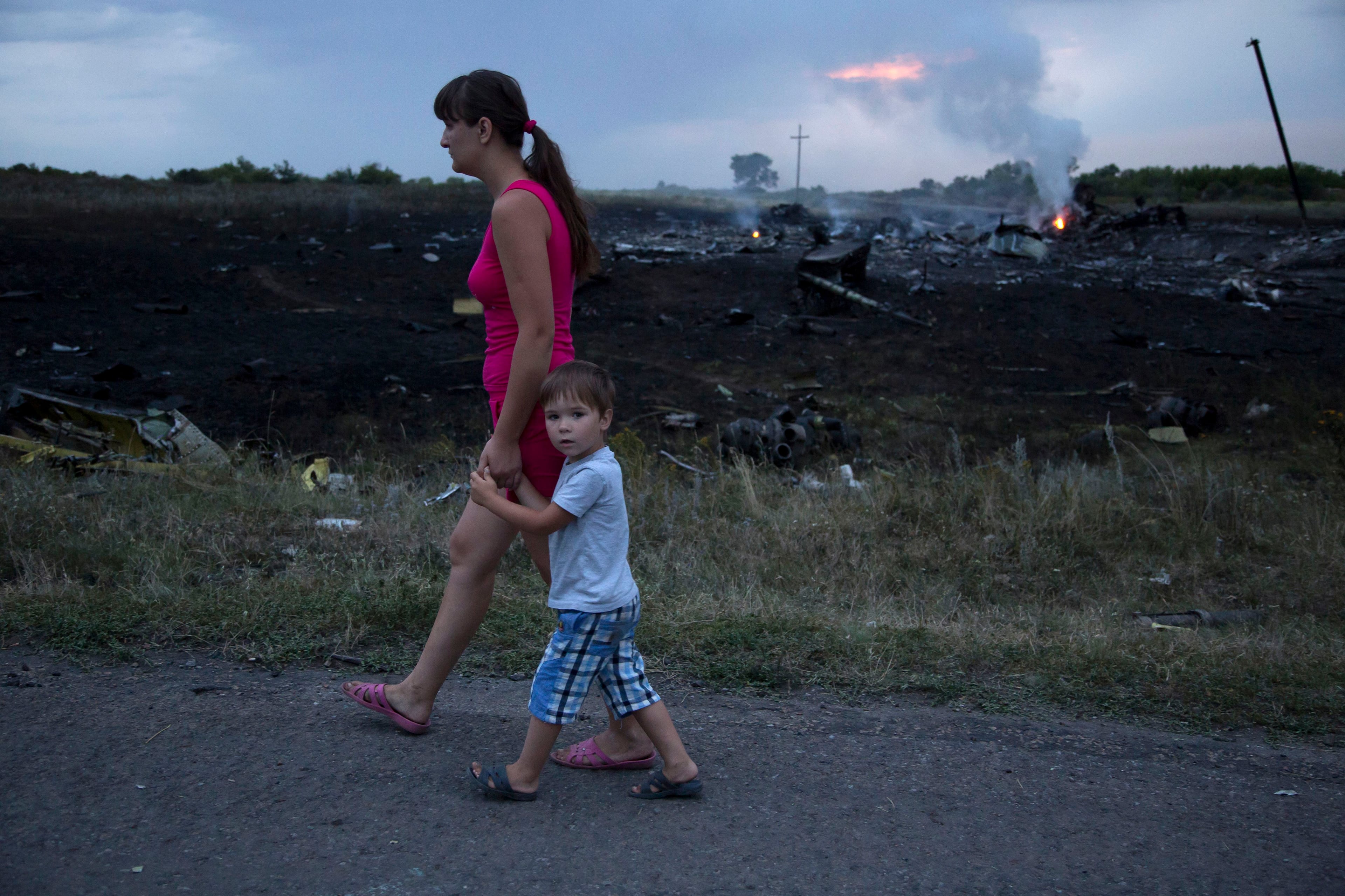 A woman with a child walks past the crash site of a passenger plane near the village of Grabovo, Ukraine, Thursday, July 17, 2014. Ukraine said a passenger plane carrying 295 people was shot down Thursday as it flew over the country, and both the government and the pro-Russia separatists fighting in the region denied any responsibility for downing the plane. (AP Photo/Dmitry Lovetsky)