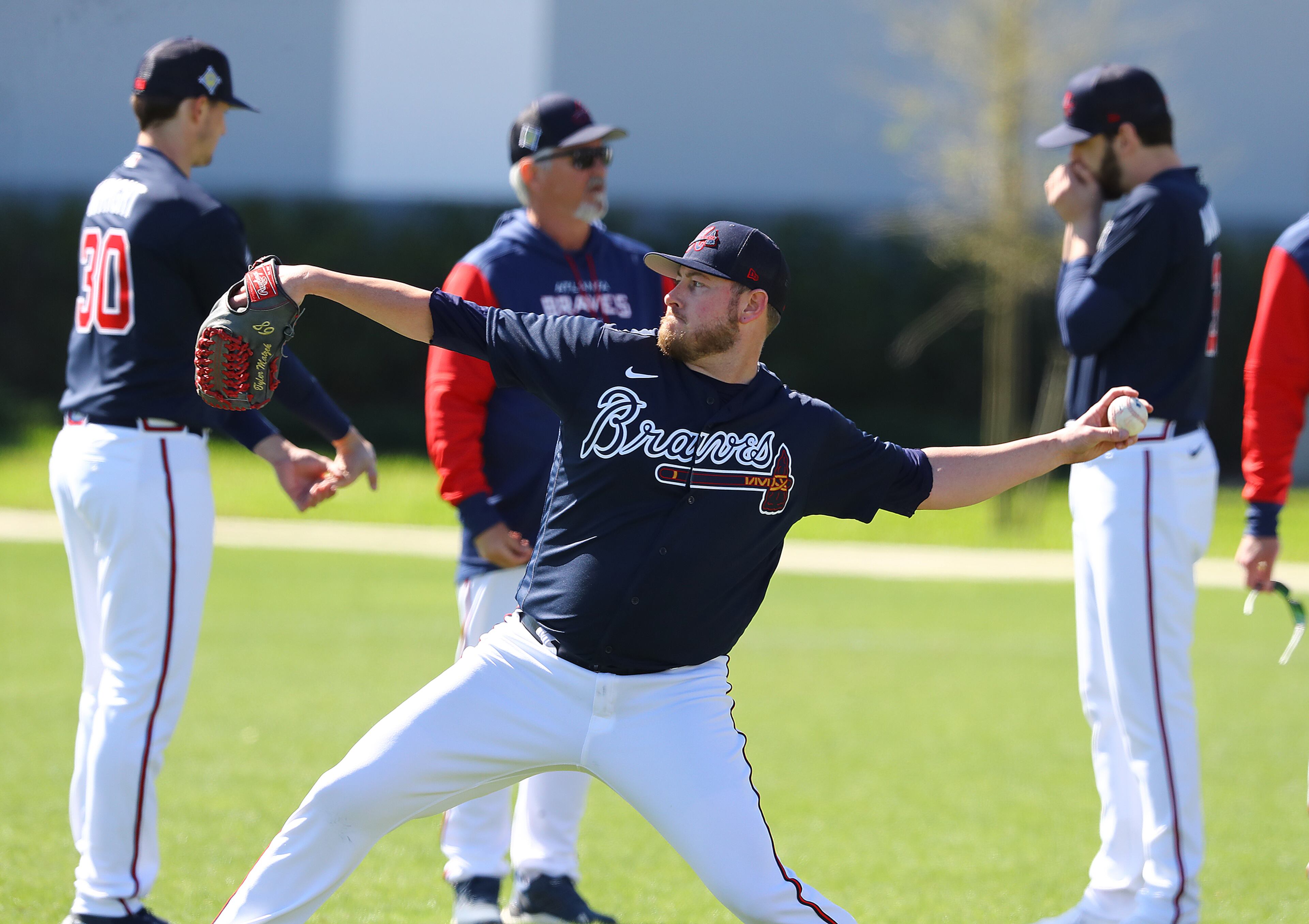 Braves pitcher Tyler Matzek loosens up his arm while Kyle Wright (left) and Ian Anderson (right) confer with pitching coach Rick Kranitz the day players have to report for spring training at CoolToday Park on Sunday, March 13, 2022, in North Port. The team’s first official workout is scheduled for Monday. “Curtis Compton / Curtis.Compton@ajc.com”`