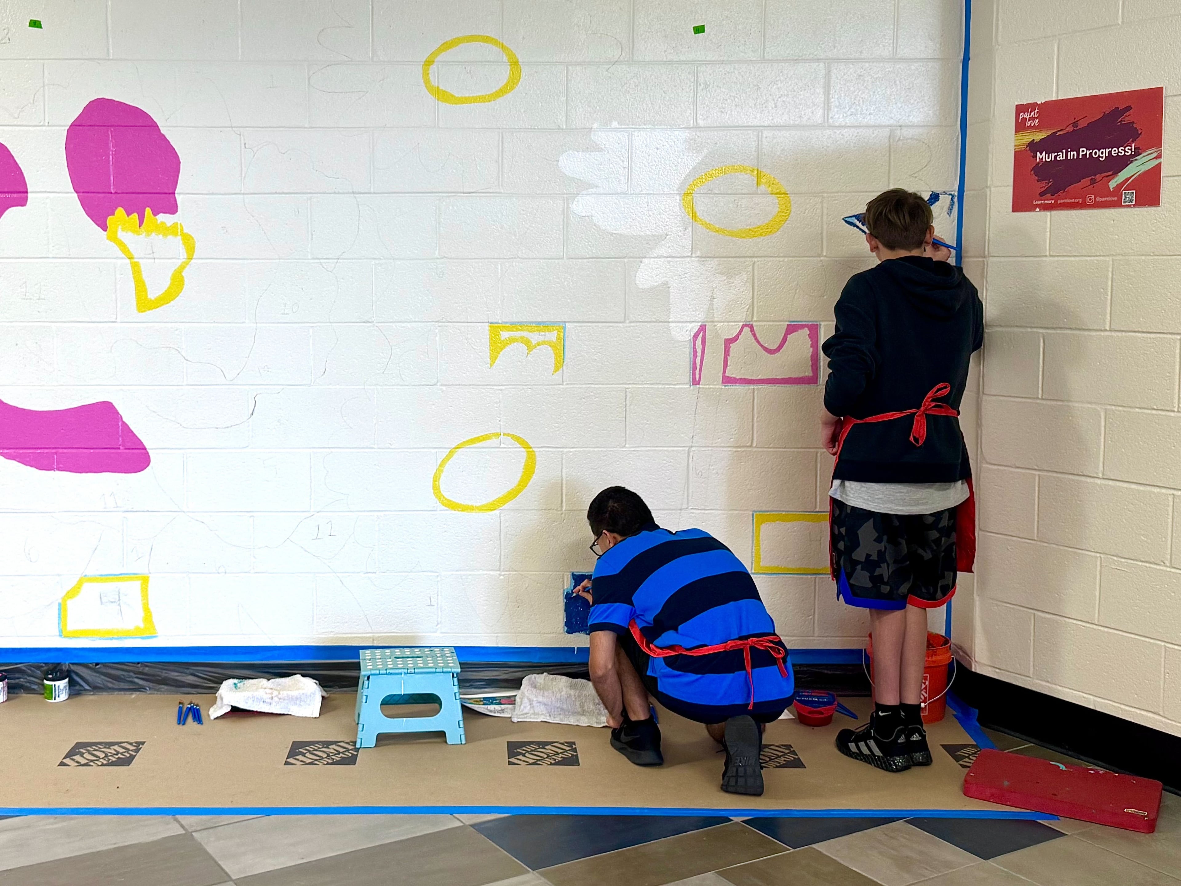 Students help paint flower petals outlined on a wall inside Apalachee High School. The flowers are part of a new mural designed to brighten a hallway near the site of 2024's school shooting. (Courtesy of Paint Love)