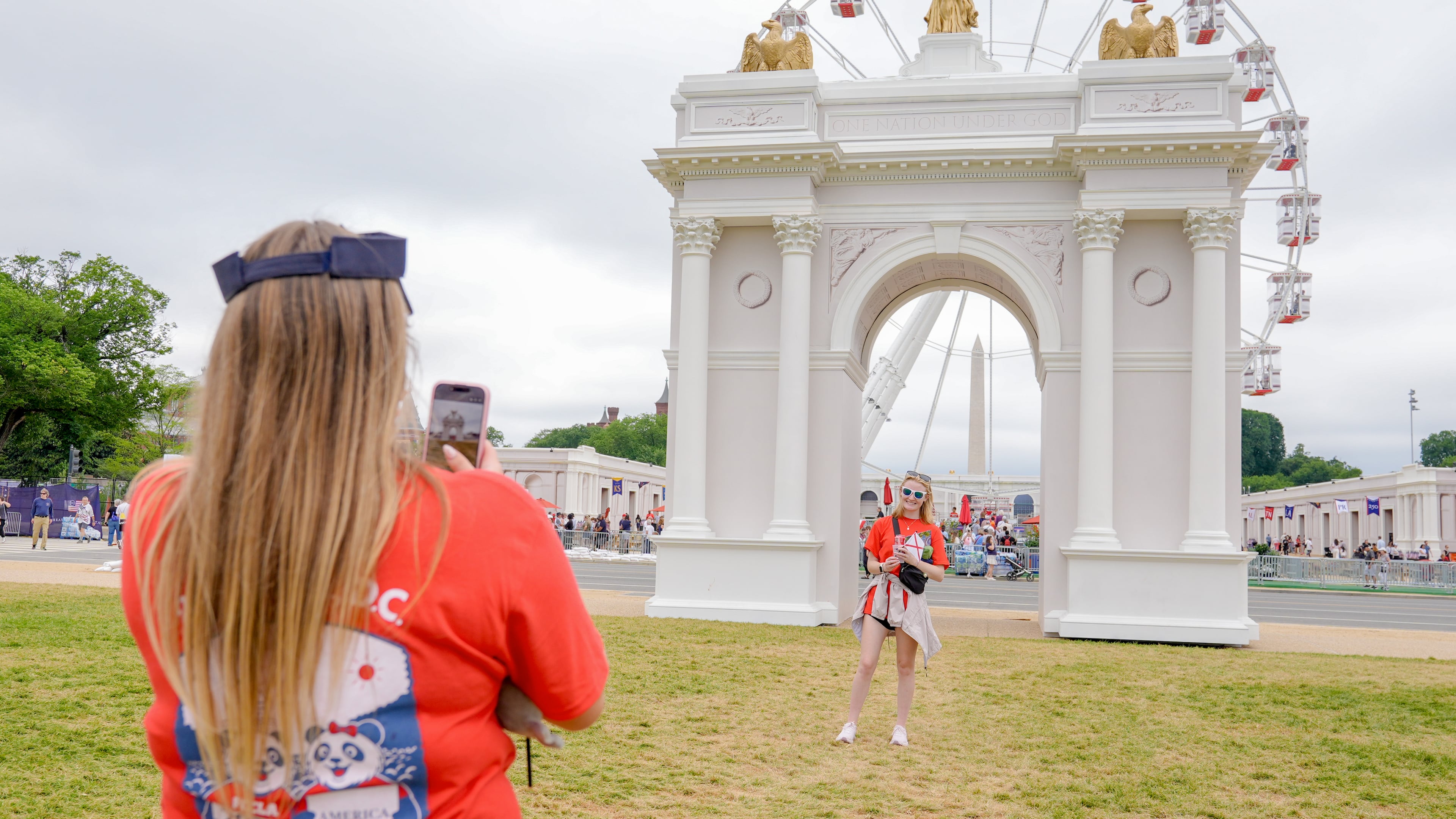 Visitors take photos at the Great American State Fair on the National Mall, with the ferris wheel and a model of the triumphal arch in the background, Thursday, July 9, 2026, in Washington. (AP Photo/Mariam Zuhaib)