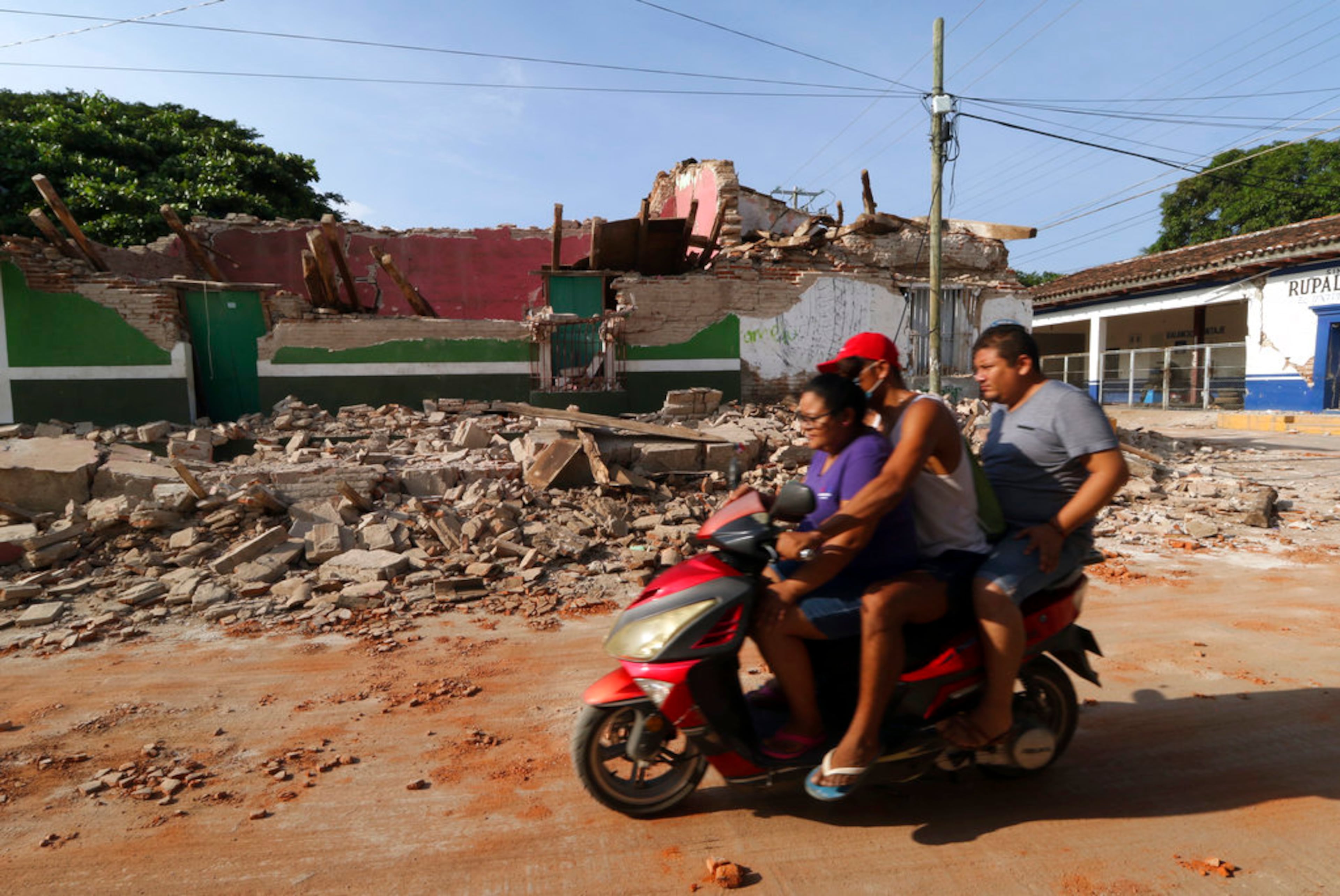 Residents drive by a collapsed building felled by a massive earthquake, in Juchitan, Oaxaca state, Mexico, Friday, Sept. 8, 2017. One of the most powerful earthquakes ever to strike Mexico has hit off its southern Pacific coast, killing at least 32 people, toppling houses, government offices and businesses. (AP Photo/Luis Alberto Cruz)