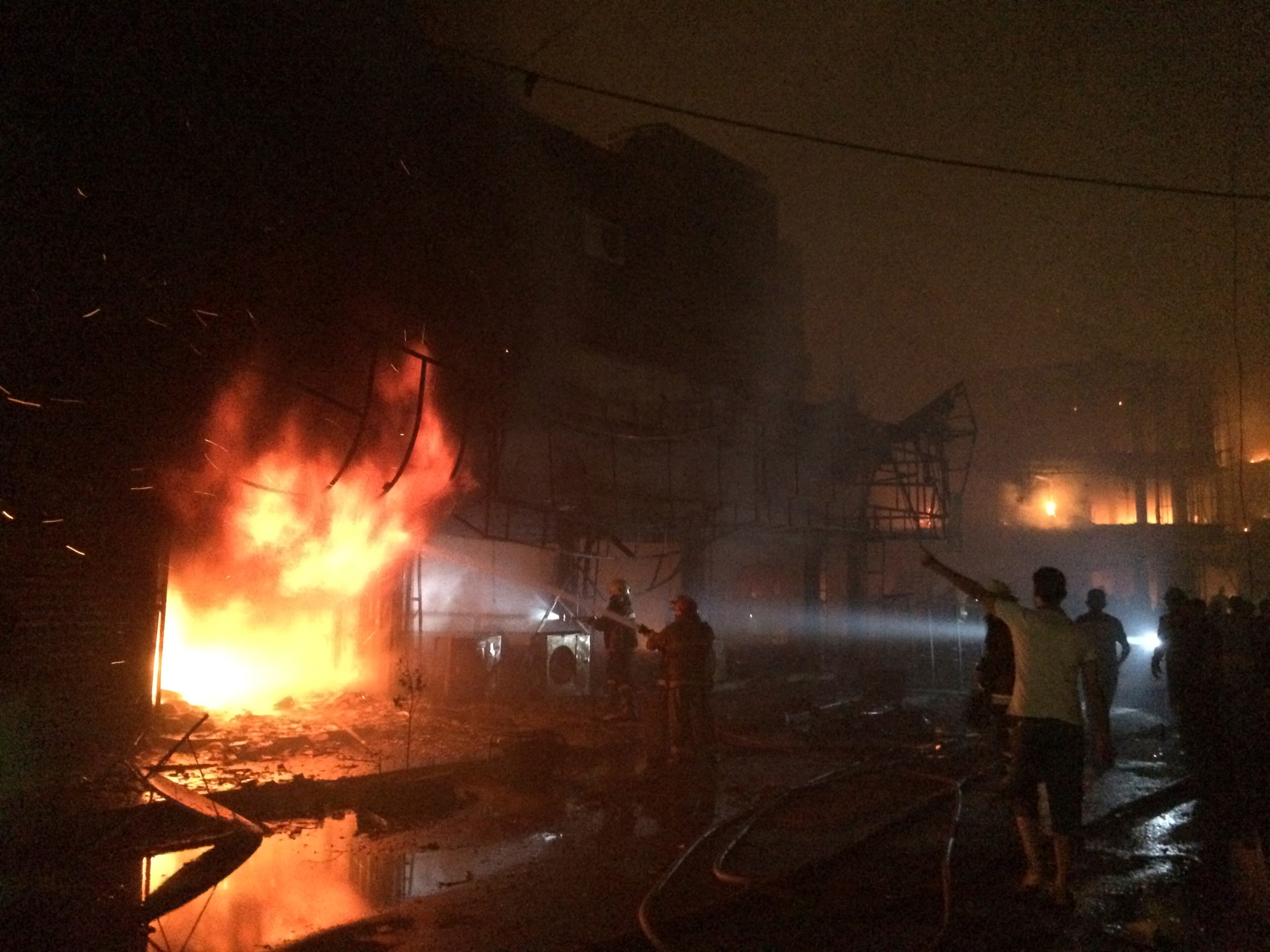 Iraqi firefighters extinguish a fire as civilians gather after a car bomb at a commercial area in Karada neighborhood, Baghdad, Iraq, early Sunday, July 3, 2016. Bombs went off early Sunday in two crowded commercial areas in Baghdad. (AP Photo/Hadi Mizban)