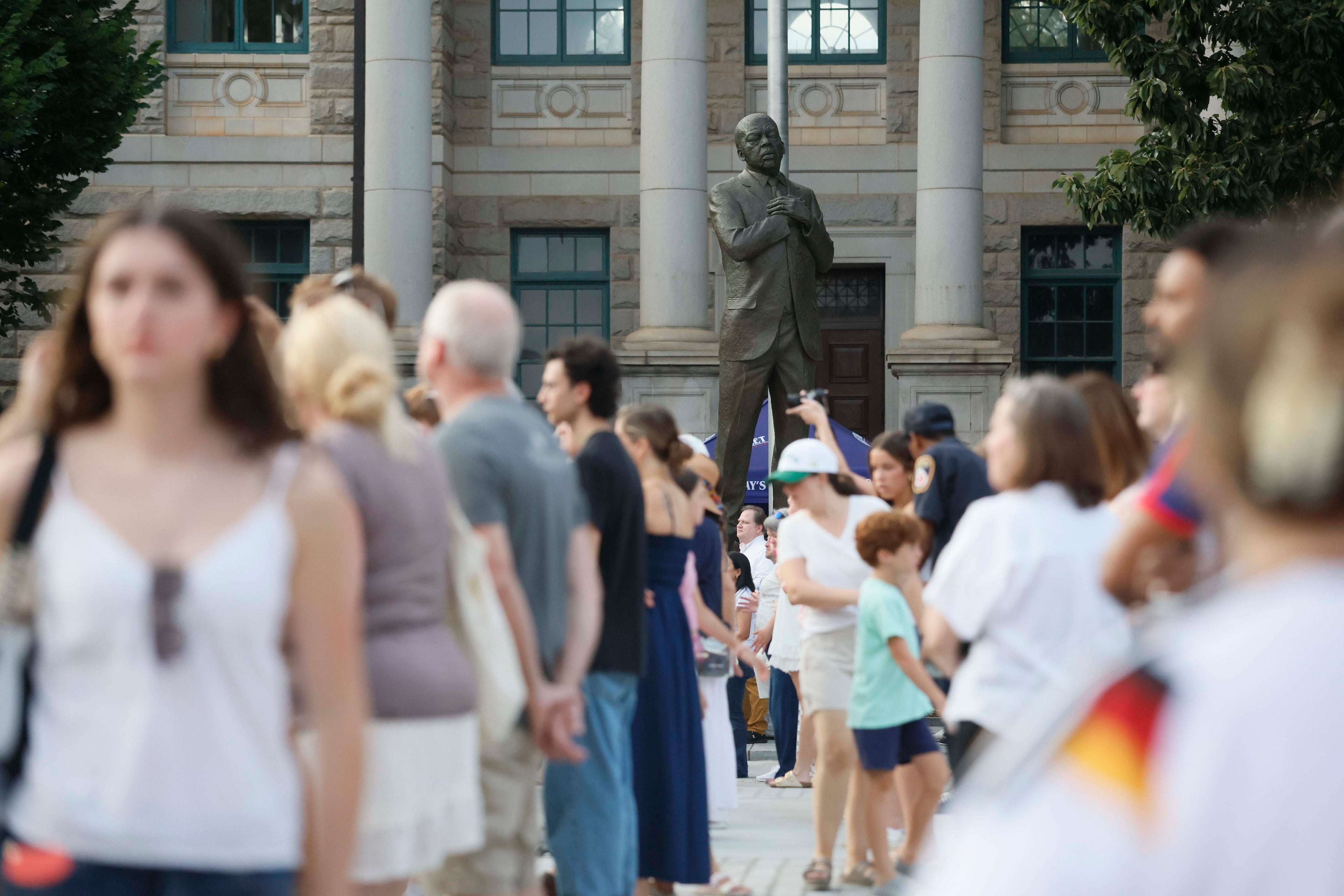 Festivalgoers walk around Decatur Square, with a statue of the late Congressman John Lewis in the background, during the Decatur WatchFest music series on Thursday, June 25, 2026. (Miguel Martinez/AJC)