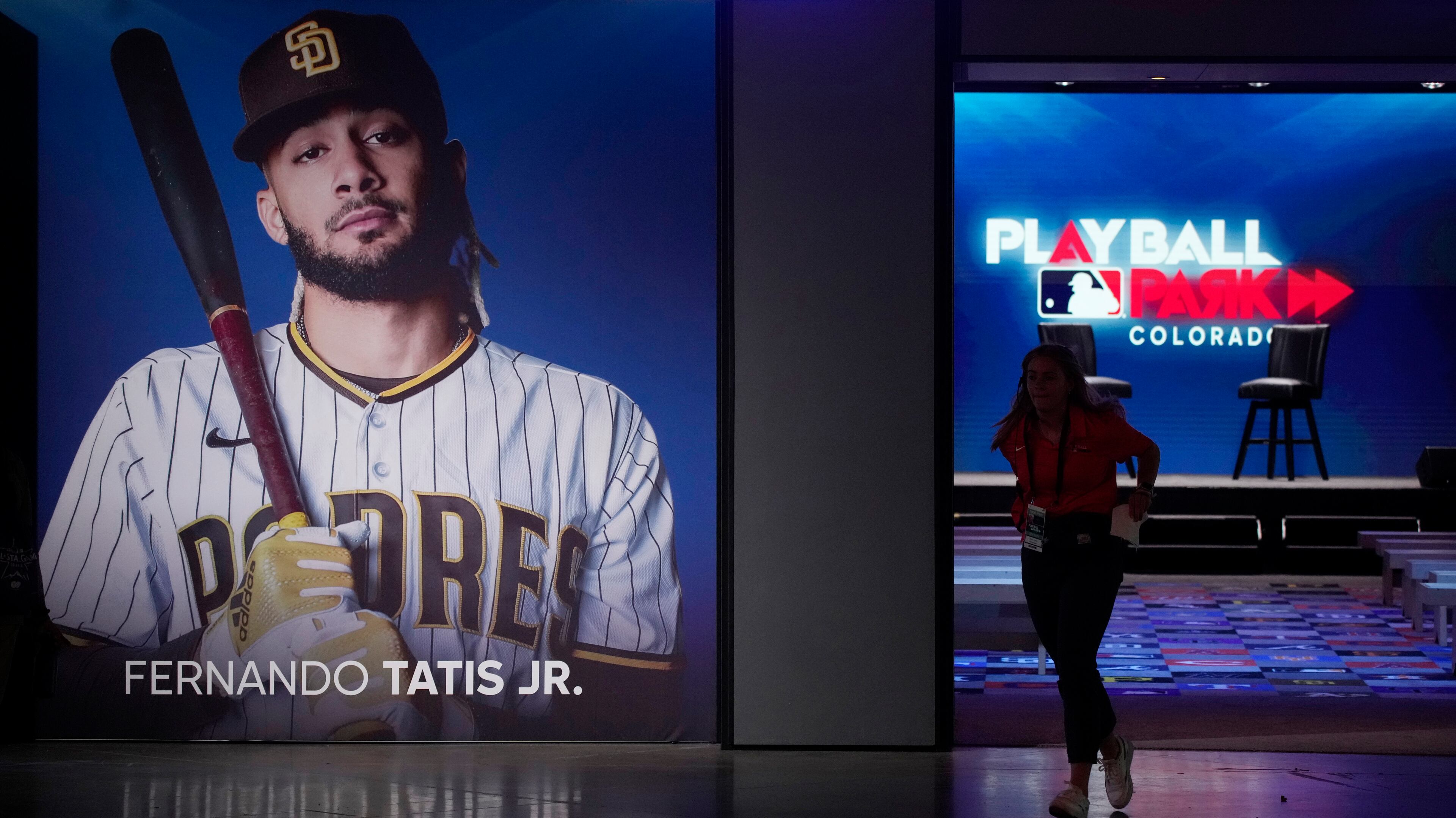 A worker runs out of the clubhouse exhibit and past a photograph of San Diego Padres shortastop Fernando Tatis Jr. at the Play Ball Park exhibit at the Colorado Convention Center staged by Major League Baseball as part of the festivities leading up to the All Star Game Friday, July 9, 2021, in Denver. The convention center has been turned into a paradise for baseball aficionados complete with batting cages, an onsite home run derby, items from the Hall of Fame and countless merchandise for sale for baseball fans from far and near at the store.