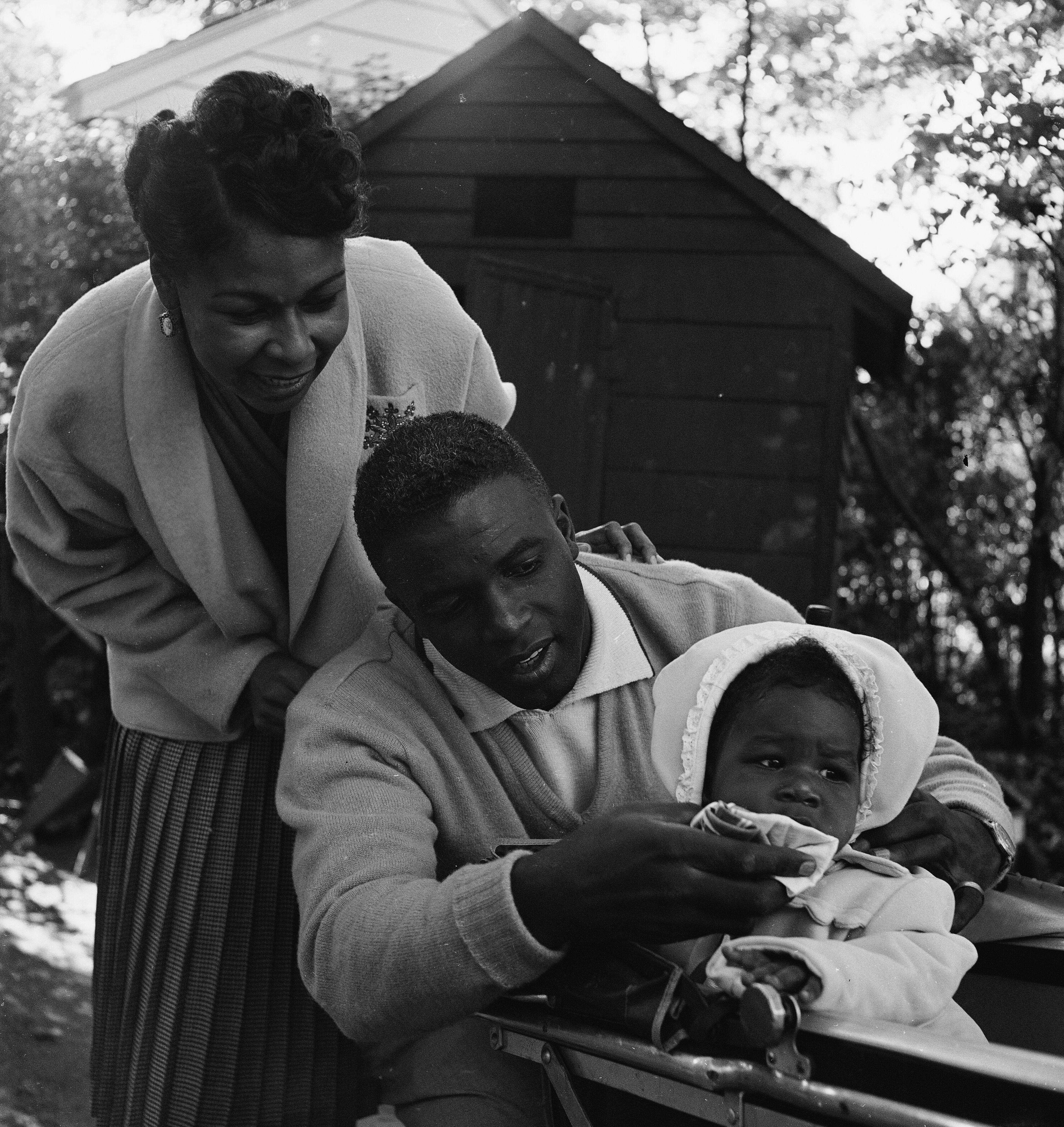 American baseball player Jackie Robinson (1919 - 1972) tends to his daughter Sharon in her baby carriage as wife Rachel looks on in the backyard of their home in Stamford, Connecticut, circa 1951. (Photo by Hulton Archive/Getty Images)