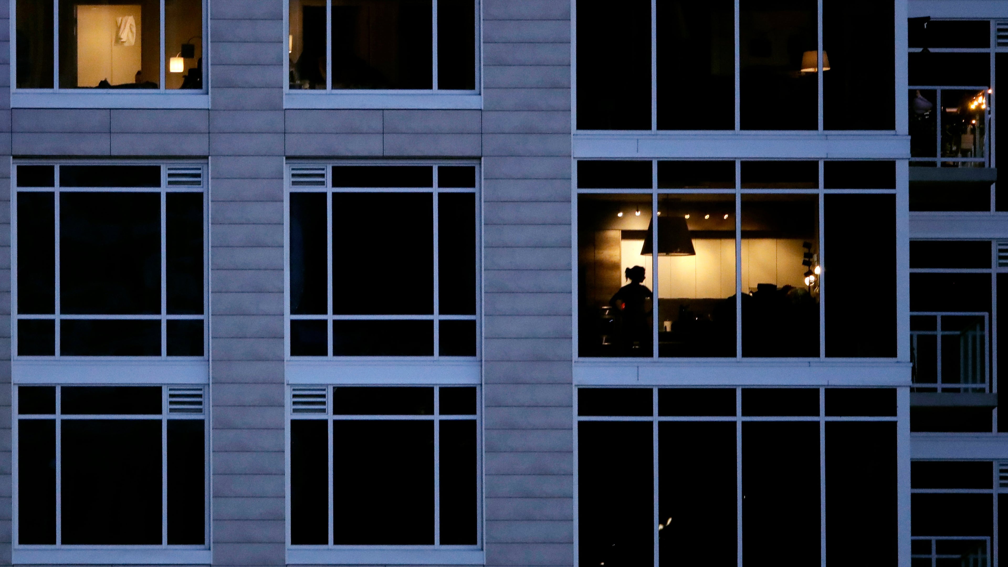 FILE - A person looks out of a window in an apartment building in Kansas City, Mo., May 3, 2020. (AP Photo/Charlie Riedel, File)