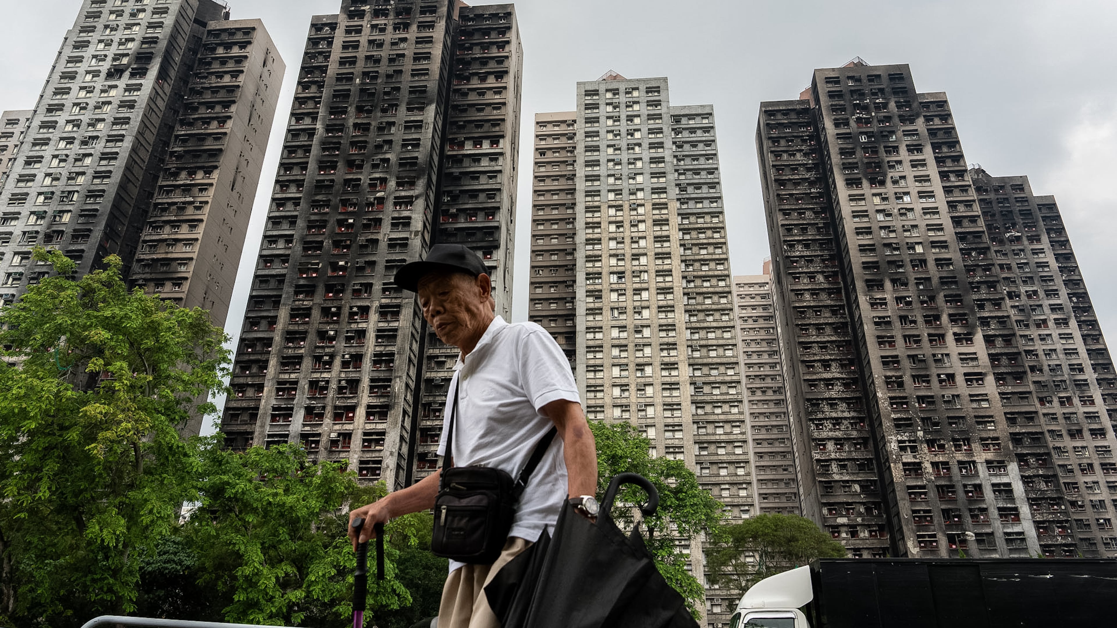 FILE -A person walks past fire-ravaged residential towers of the Wang Fuk Court apartment complex after the deadly fire in November, in the Tai Po district of Hong Kong, April 20, 2026. (AP Photo/Chan Long Hei, File)