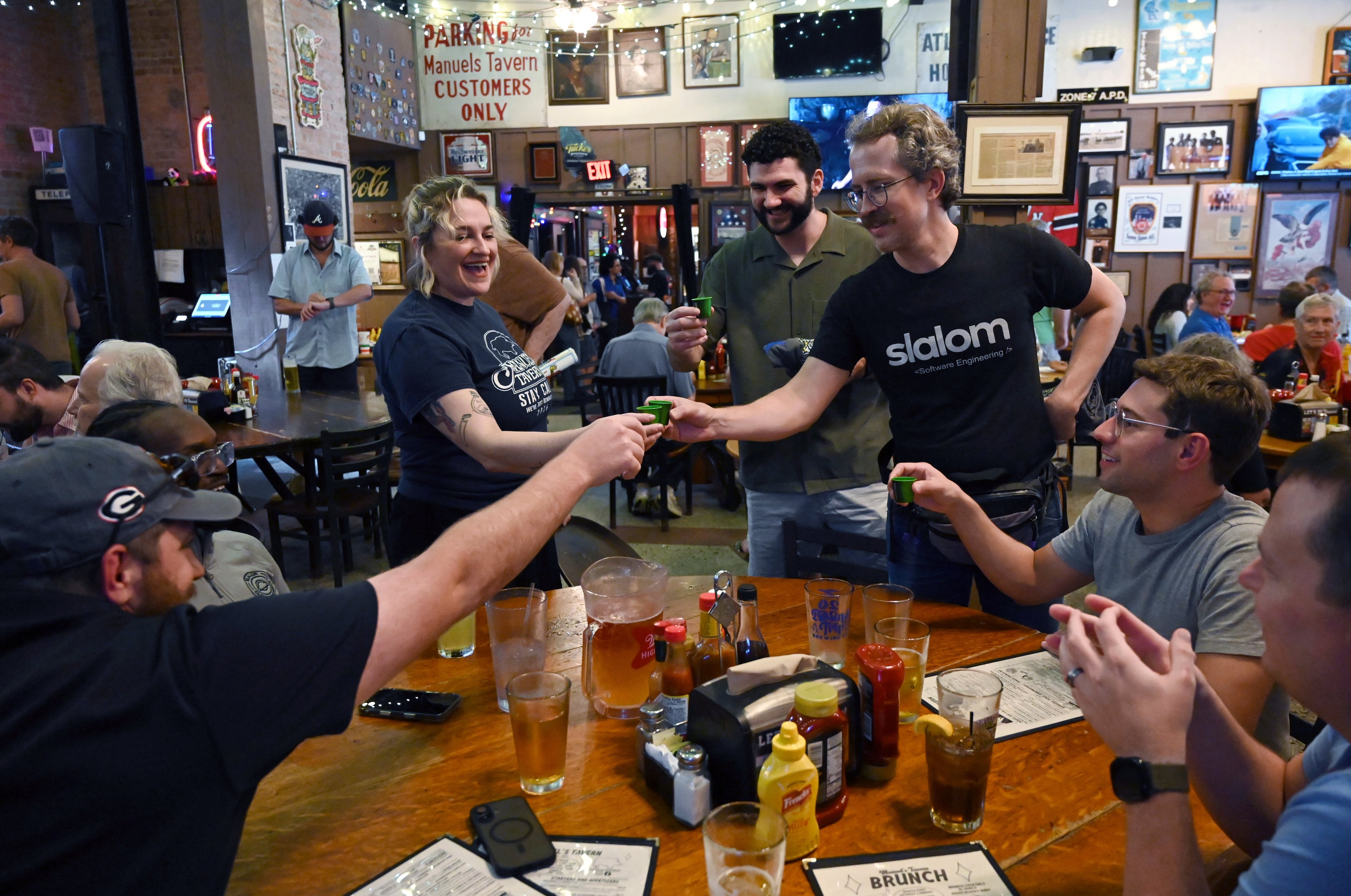 Megan Maloof (left, standing), granddaughter of the original owner, shares a toast with guests during Manuel’s Tavern’s 70th anniversary celebration on Thursday, Aug. 6, 2026, in Atlanta. (Hyosub Shin/AJC)