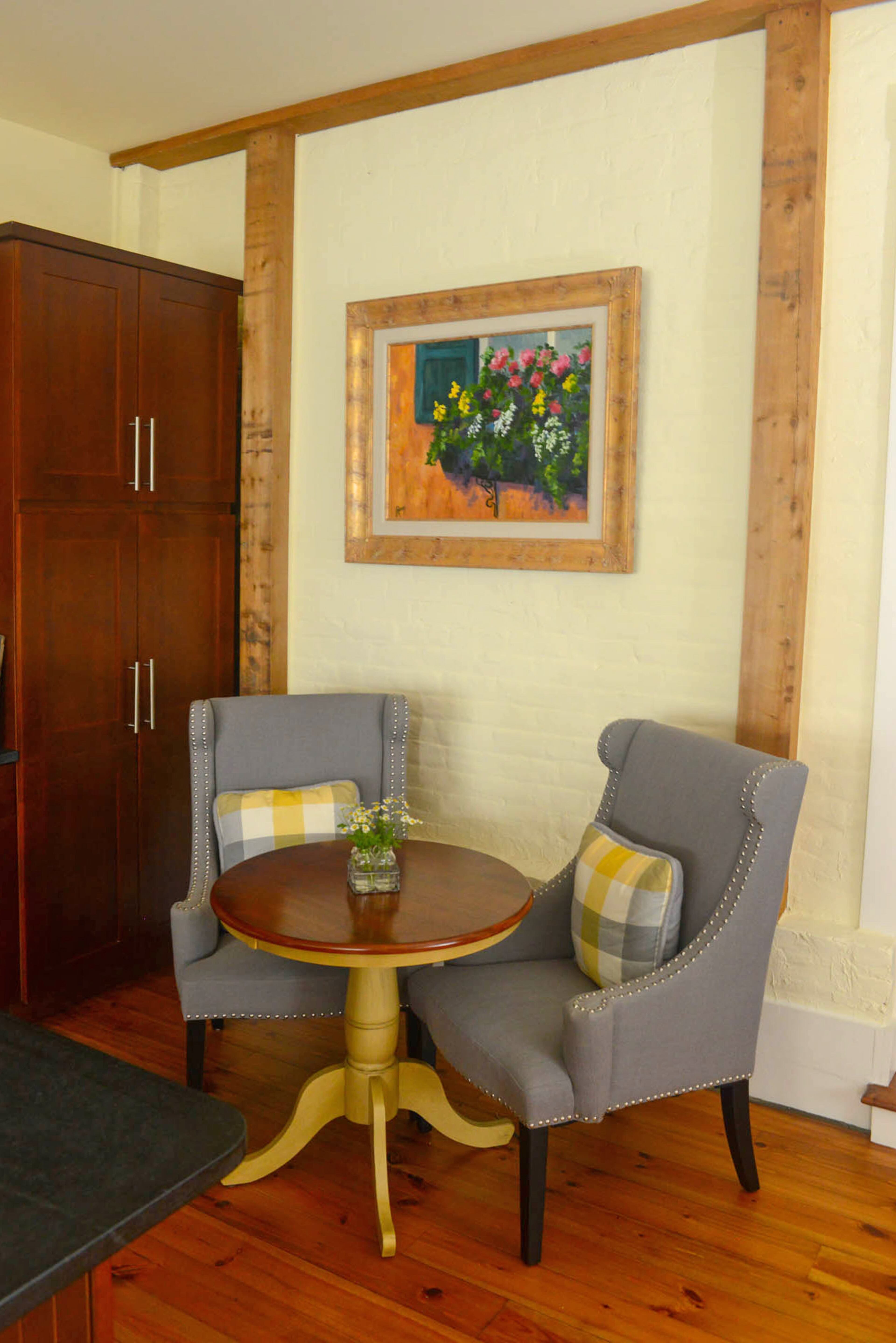 The kitchen holds a nook with gray chairs and a table purchased from Kohl's website. The beams, which were already part of the house, frame a painting by Jean Raney, a friend of Dee.