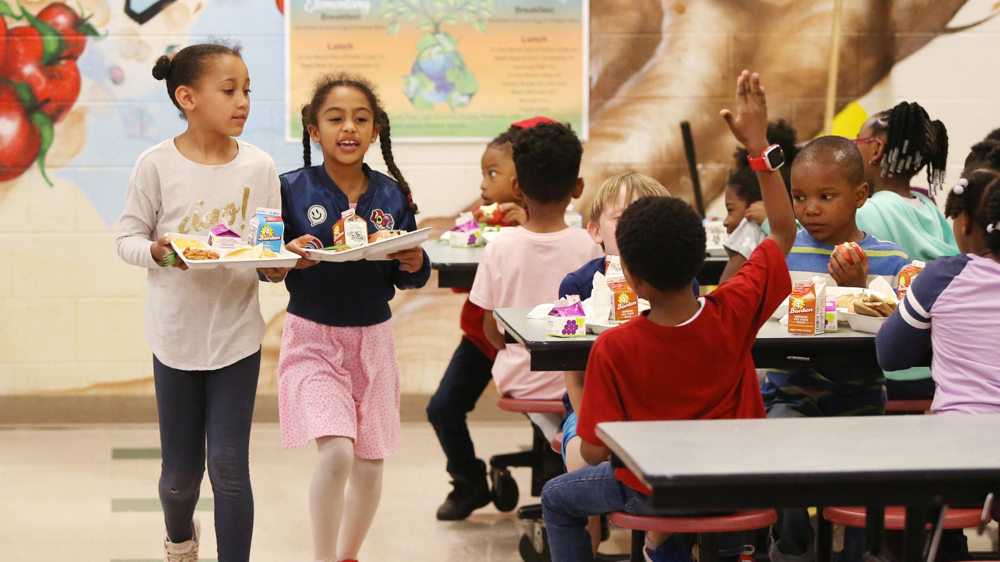 Savannah Lynn, left, and Gabriella Bolden, first-grade students, walk to their lunch table at Burgess-Peterson Academy in Atlanta on Friday. To celebrate Earth Day, Burgess-Peterson Academy was one of about 15 Atlanta schools that used biodegradable products, such as trays and forks. EMILY HANEY / emily.haney@ajc.com