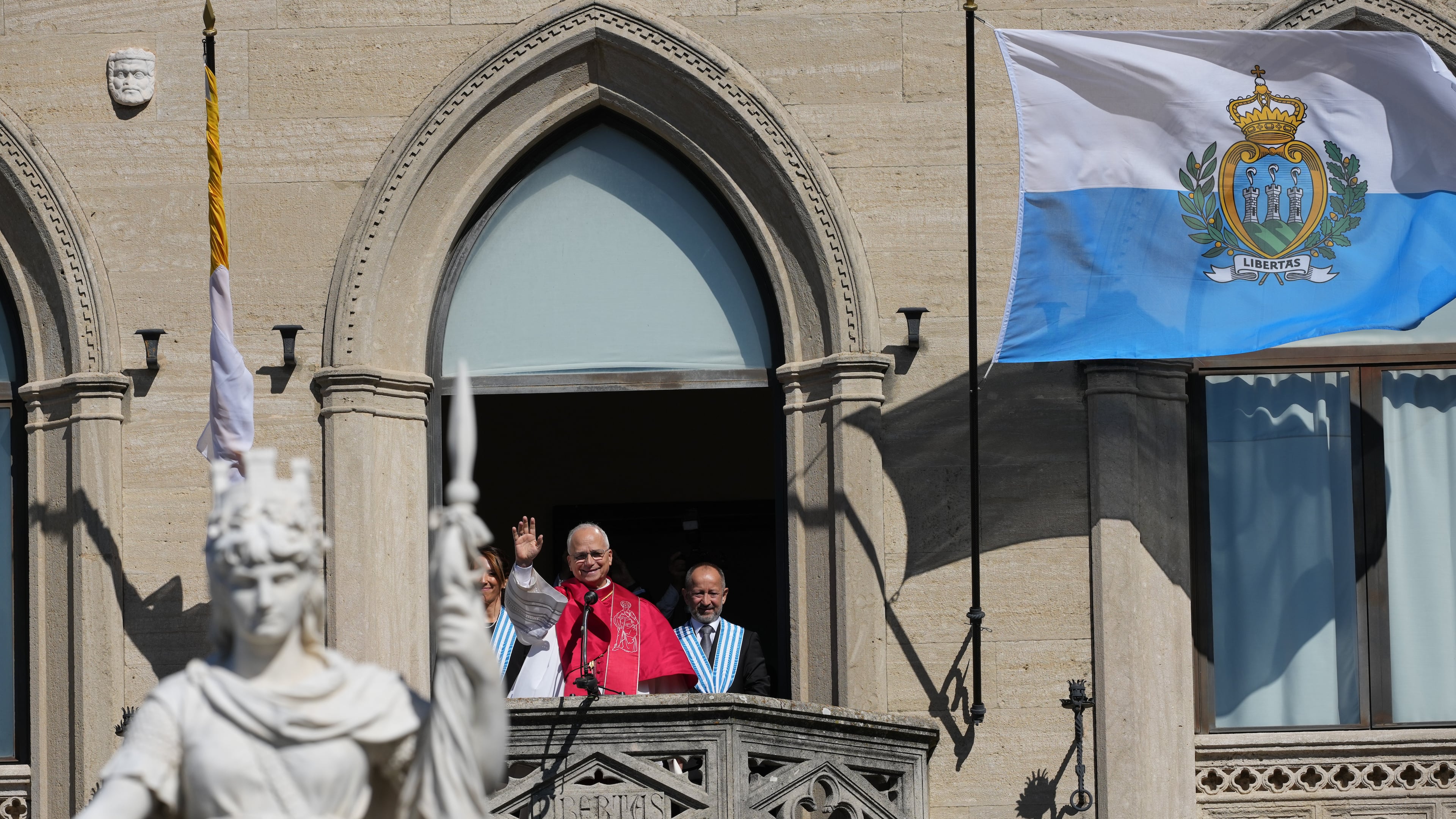 Pope Leo XIV, center, flanked by Captains Regent Alice Mina, left, and Vladimiro Selva, waves to faithful from the balcony of Palazzo Pubblico (City Hall) during his visit to San Marino, Saturday, Aug. 22, 2026. (AP Photo/Andrew Medichini)