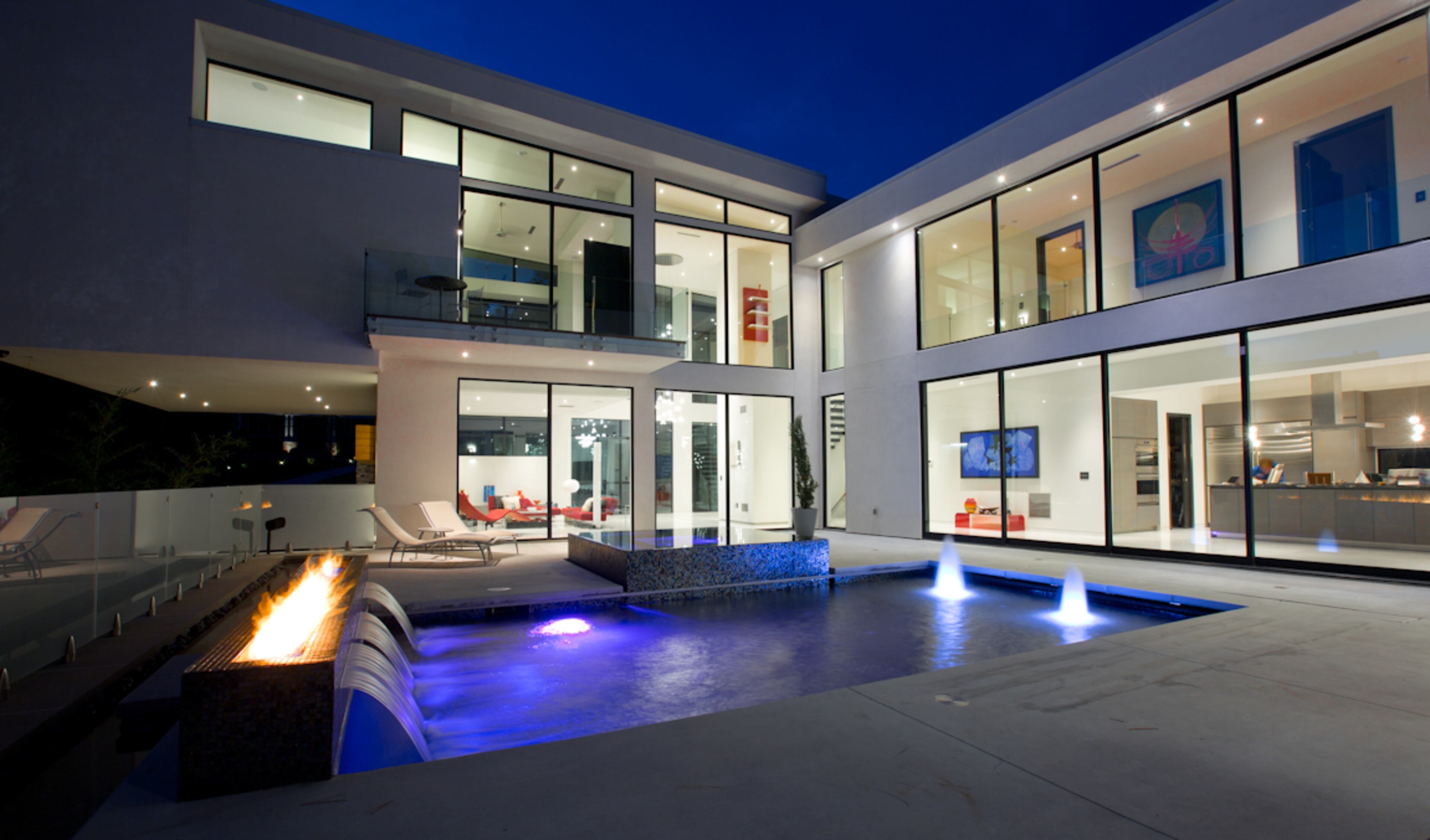 Prominent glass façade wraps around the saltwater pool deck featuring firewall, water sheers, and front and rear water features that provide the serenity of falling water. Text by Sarah Kiomall