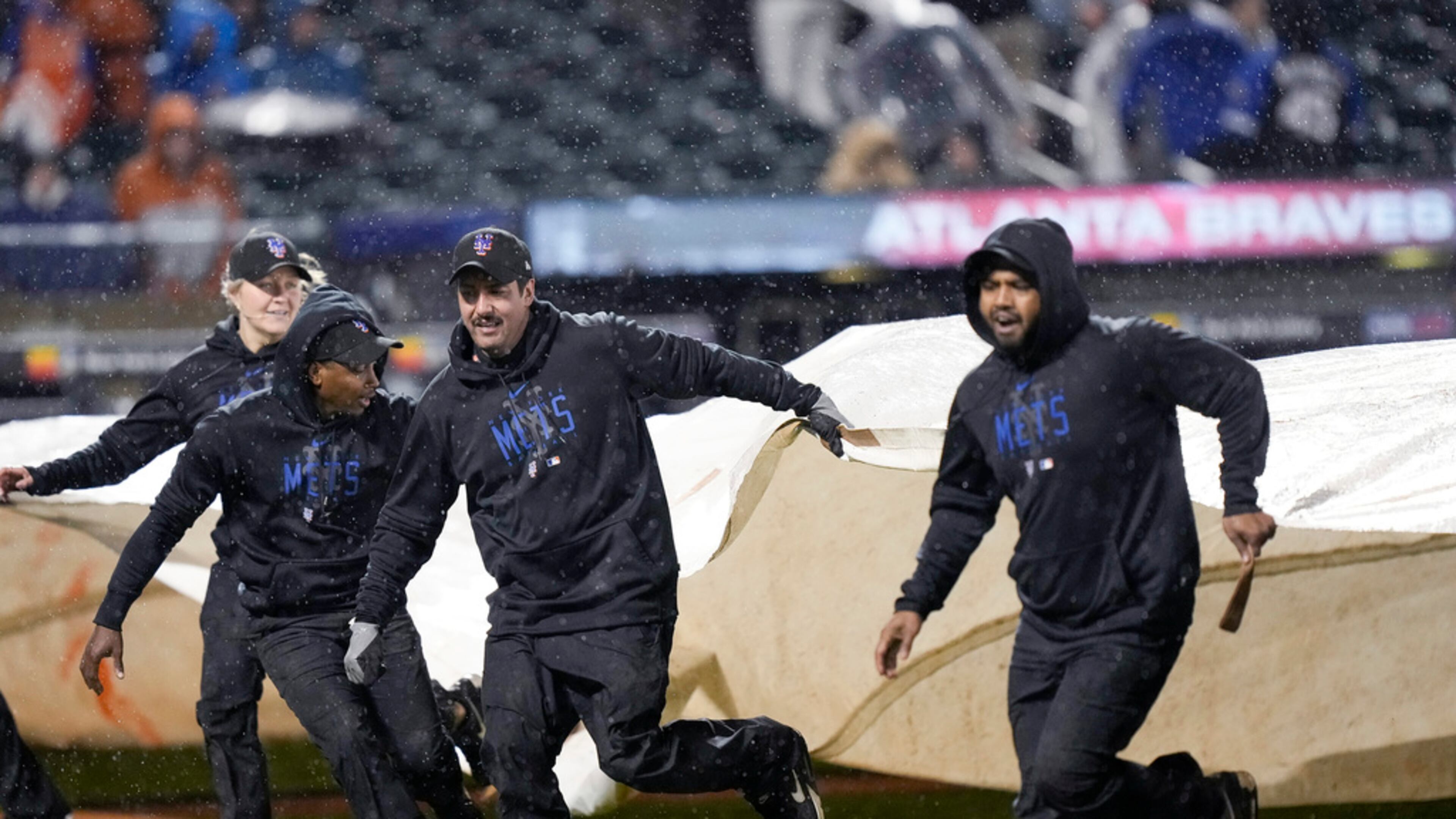Members of the grounds crew cover the field with the tarp during a rain delay after the fifth inning of a baseball game between the New York Mets and the Atlanta Braves, Friday, April 28, 2023, in New York. (AP Photo/Bryan Woolston)