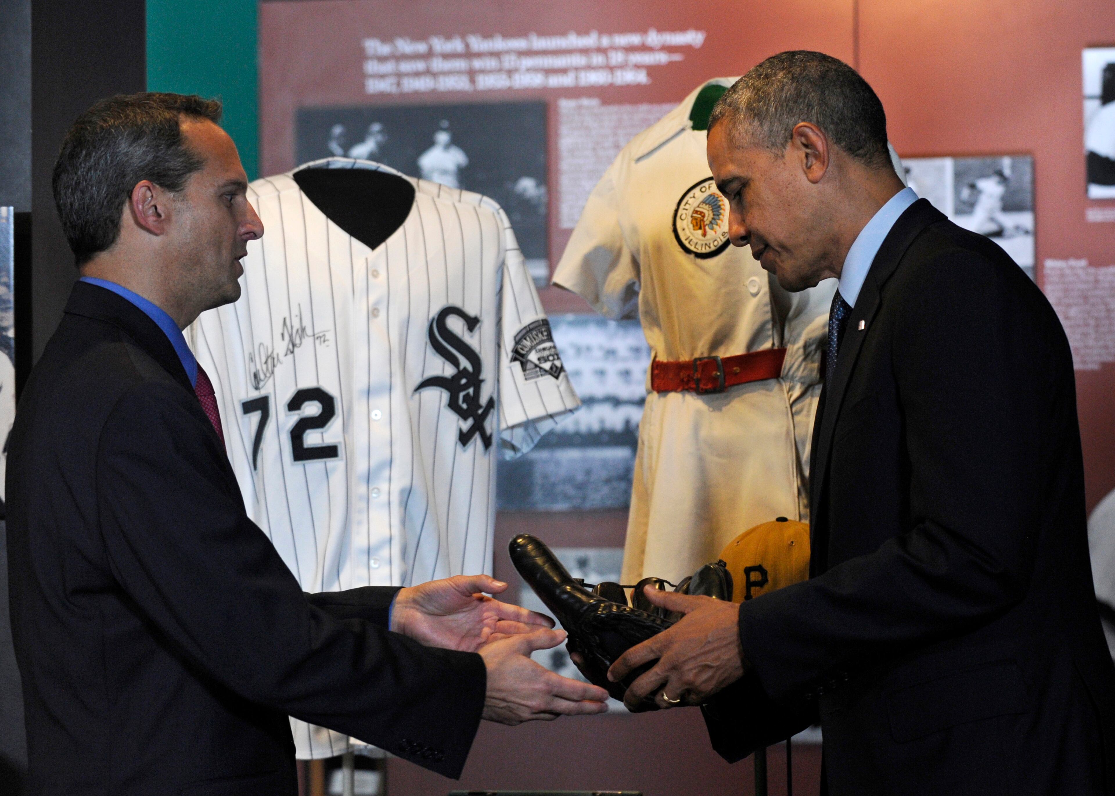 President Barack Obama is handed Joe DiMaggio's well-worn baseball glove by Baseball Hall of Fame President Jeff Idelson during a tour the Baseball Hall of Fame in Cooperstown, N.Y., Thursday, May 22, 2014. Obama visited the museum to highlight tourism and steps to help spur international visits to the 50 states. Obama said the overall U.S. economy and local businesses will benefit if it isn't a hassle for people from other countries to visit the U.S. and spend money at its hotels, restaurants, tourist destinations and other businesses. An autographed Carlton Fisk Chicago White Sox jersey is behind them. (AP Photo/Susan Walsh)