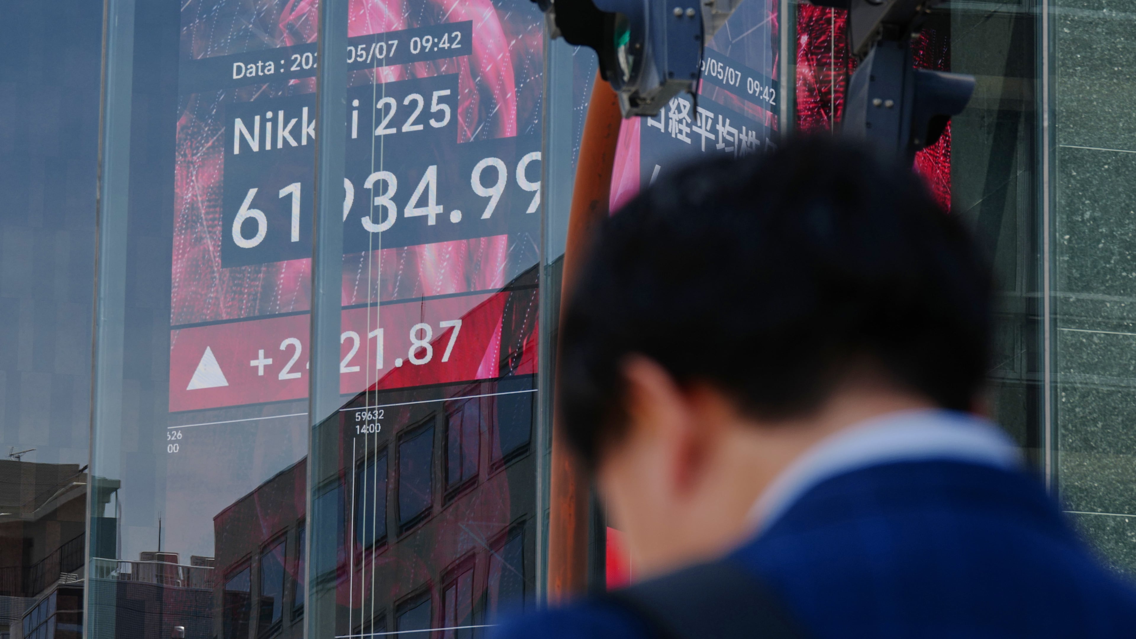 FILE - A person stands in front of an electronic stock board showing Japan's Nikkei index, seen through the glass wall of an office building in Tokyo, May 7, 2026. (AP Photo/Eugene Hoshiko, File)