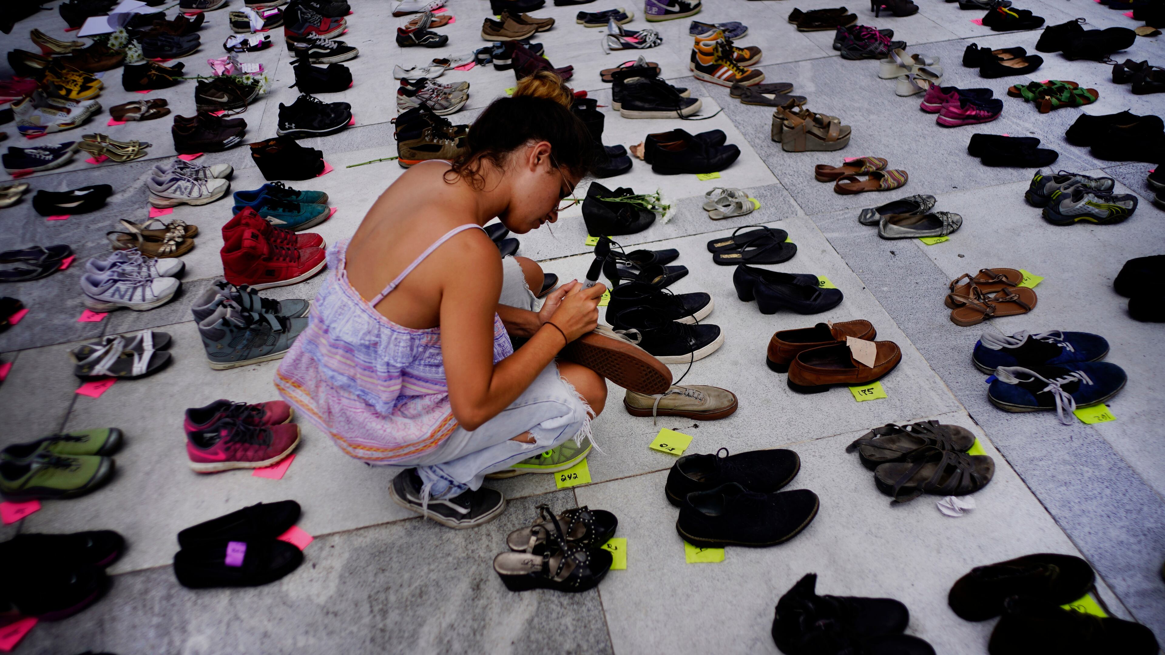 A woman places one of the hundreds of shoes in memory of those killed by Hurricane Maria in front of the Puerto Rico Capitol, in San Juan, Friday, June 1, 2018. Puerto Rico's Institute of Statistics announced that it has sued the U.S. territory's health department and demographic registry seeking to obtain data on the number of deaths following Hurricane Maria as a growing number of critics accuse the government of lacking transparency.
