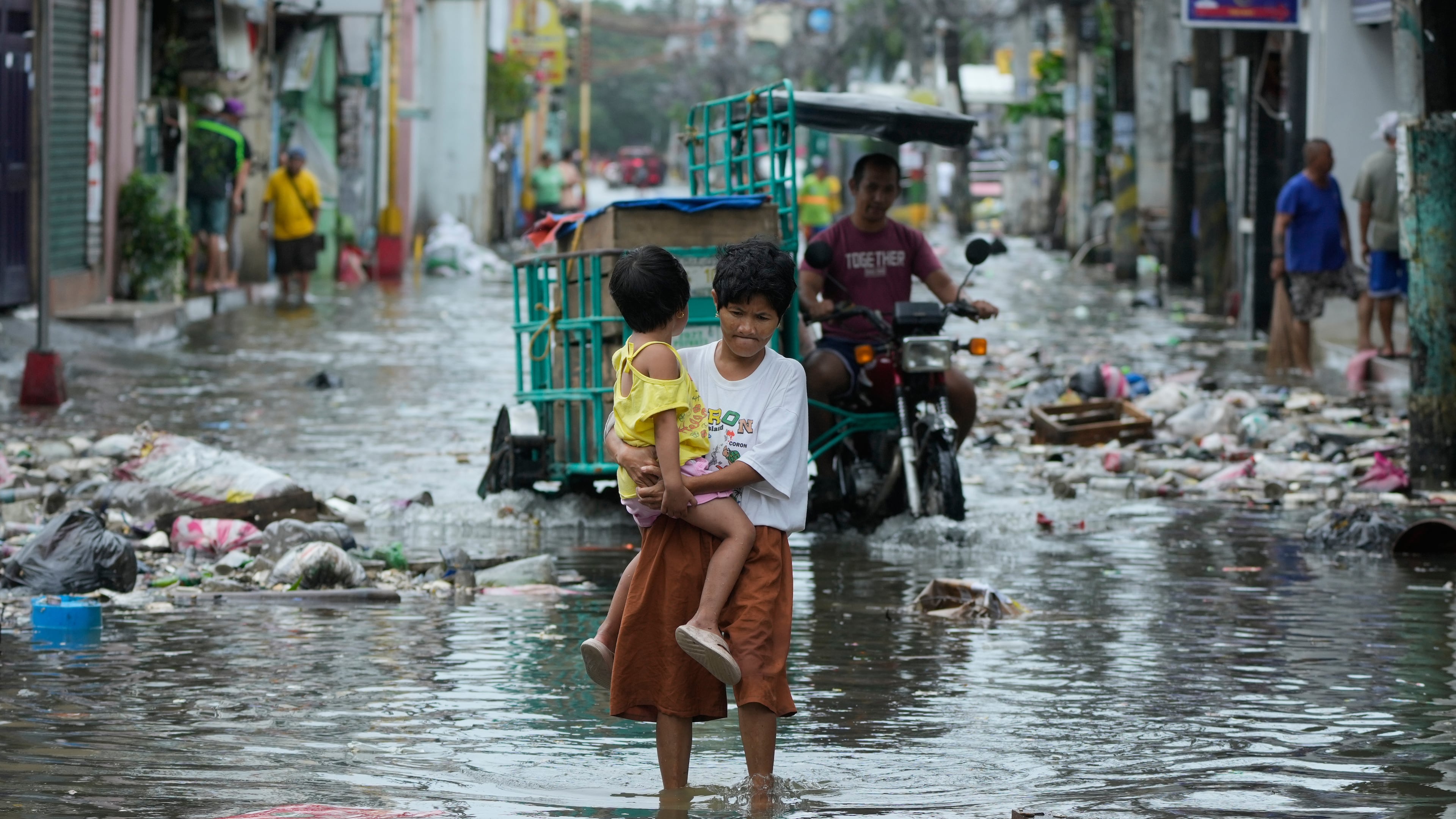 FILE - A woman and child crosses a flooded street due to Typhoon Fung-wong and high tide on Nov. 10, 2025, in Navotas, Philippines. (AP Photo/Aaron Favila, File)