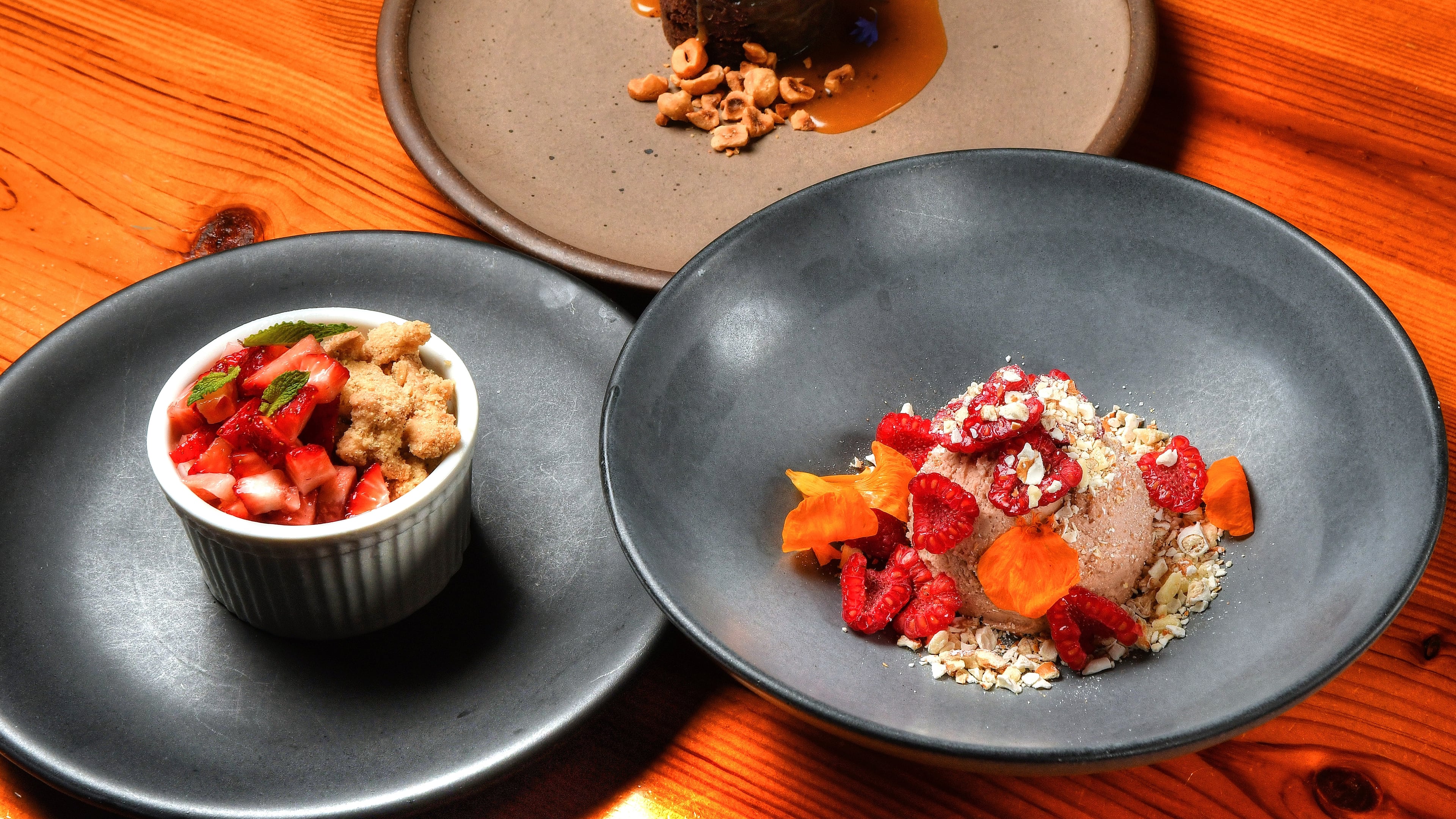 Miller Union pastry chef Claudia Martinez offers some spring-to-summer seasonal recipes: Gluten-Free Chocolate Cake With Salted Caramel and Candied Hazelnuts (top), Meyer Lemon Semifreddo With Oat Cookie Crumble and Macerated Strawberries (bottom left), and Raspberry Cheesecake Mousse With Pretzel Crunch (bottom right). Styling by Claudia Martinez / Chris Hunt for the AJC