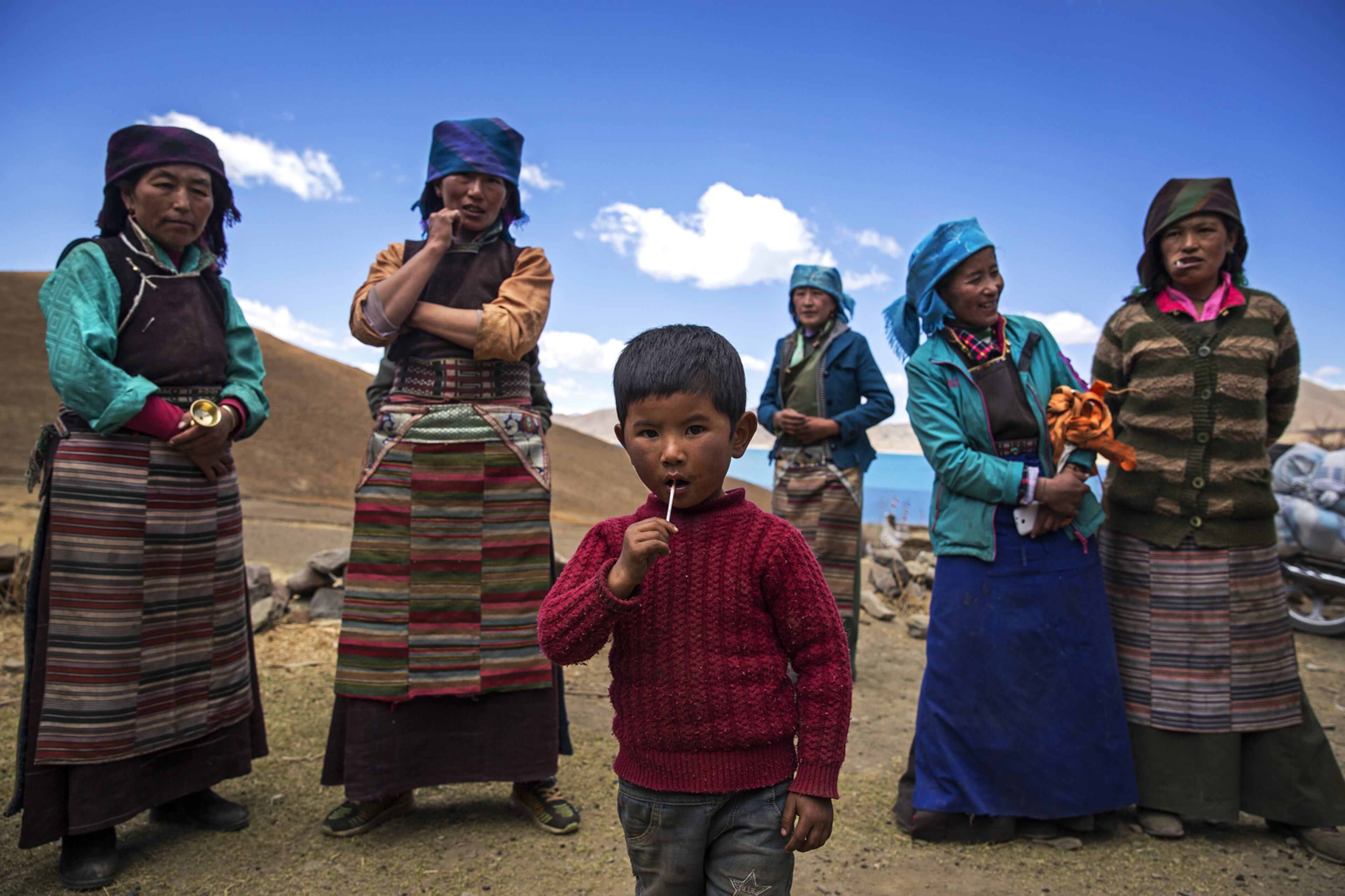 LHOKHA, CHINA - APRIL 26: A child eats a lollipop as Tibetan women stand in a village near the Yamdrok Lake on April 26, 2017 in Dongla County in the Lhokha Prefecture of Tibet Autonomous Region, China. Yamdrok Lake is one of the four largest sacred lakes in Tibet. The lake is surrounded by many snow-capped mountains and is fed by numerous small streams. (Photo by Wang He/Getty Images) *** BESTPIX ***