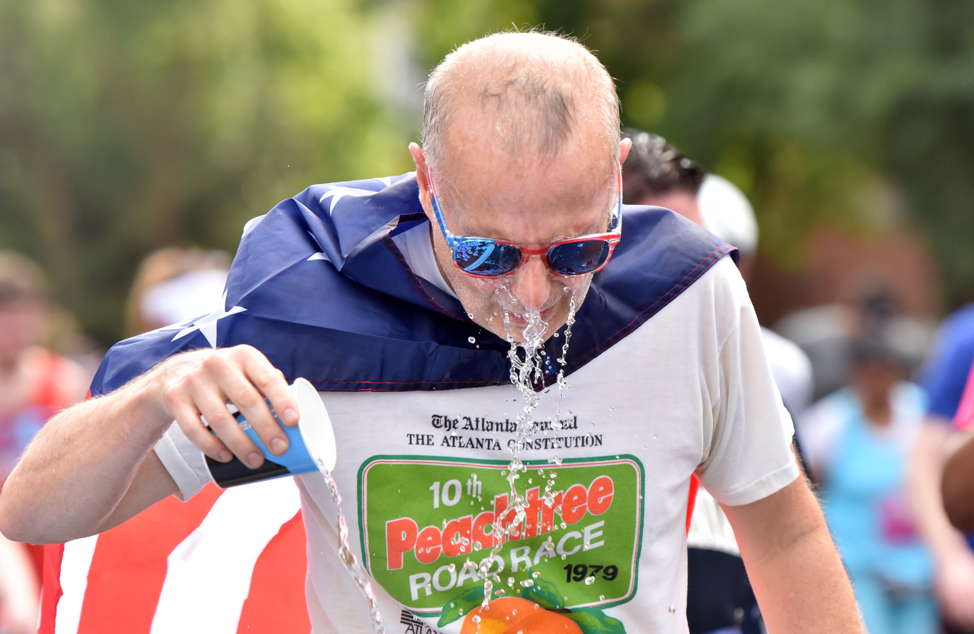 A runner cools off with a cup of water at a water station at Shepherd Center during the 50th AJC Peachtree Road Race on Thursday, July 4, 2019. (Hyosub Shin / Hyosub.Shin@ajc.com)