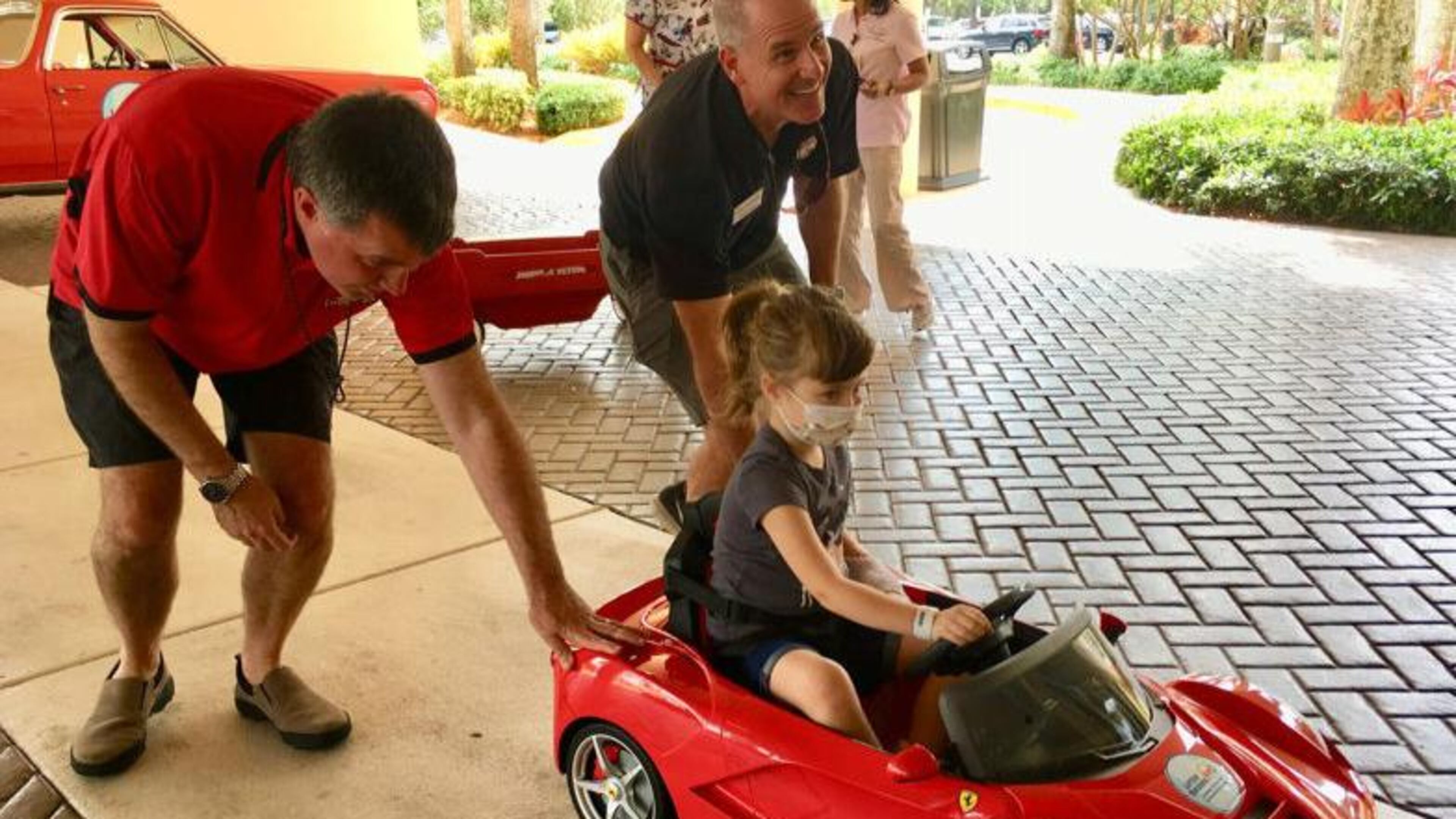 Brian Murphy, left, and Craig Kelley roll a mini-Ferrari convertible carrying 5-year-old Abigail Sporke into Palms West Hospital. Murphy and Kelley are with Little Smiles, which donated the car to the hospital's pediatric patients.