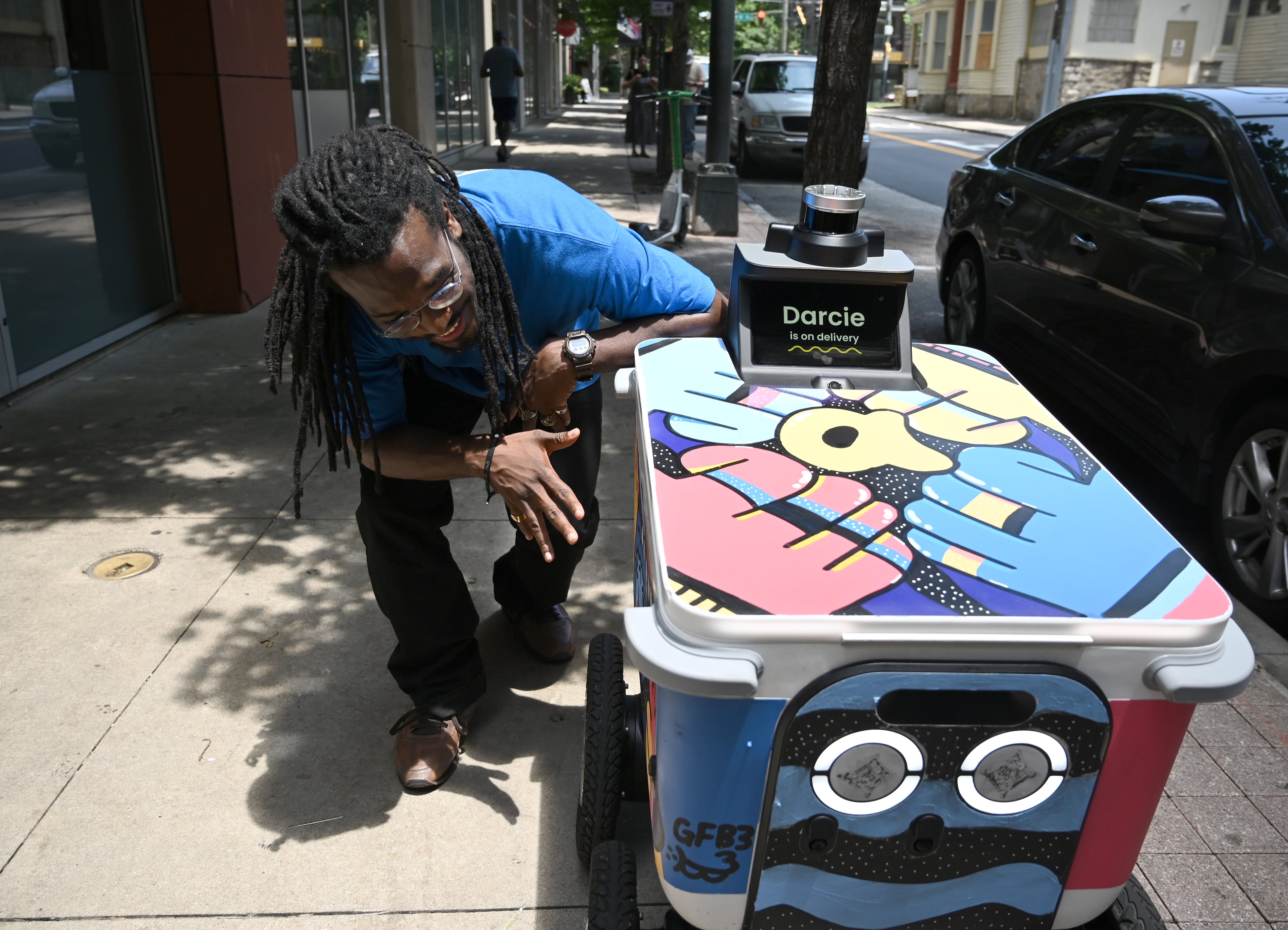 Atlanta muralist George F. Baker III shows off a food delivery robot “Darcie” that he painted outside Rreal Tacos' Midtown location, Thursday, June 26, 2025, in Atlanta. (Hyosub Shin/AJC)