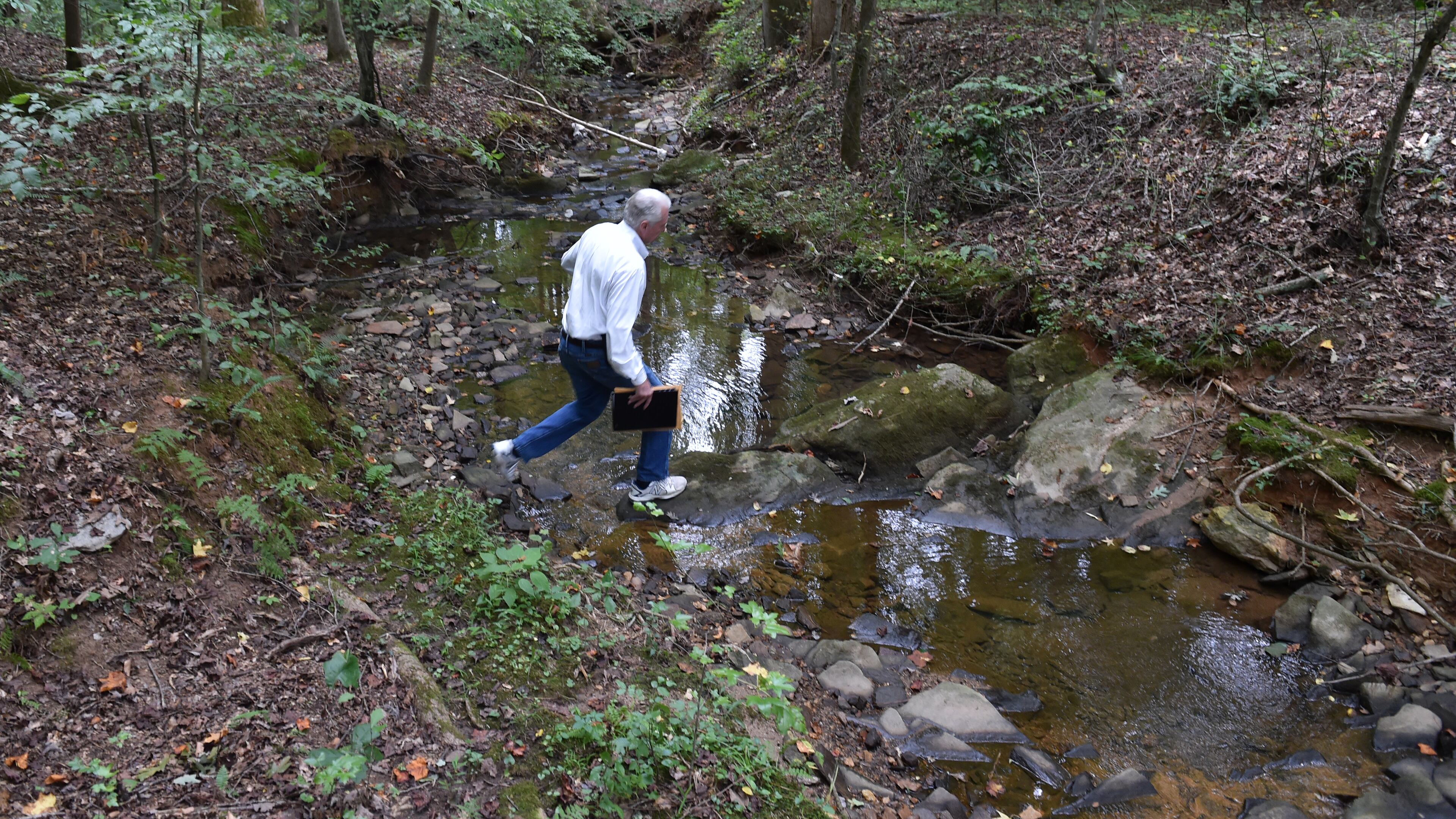 August 28, 2015 Roswell, GA: L.W. Tucker is part of a group pressing Roswell city officials to buy 53 wooded acres along Holcomb Bridge Road and preserve it as a park. Tucker crosses a creek during a tour of the property. BRANT SANDERLIN