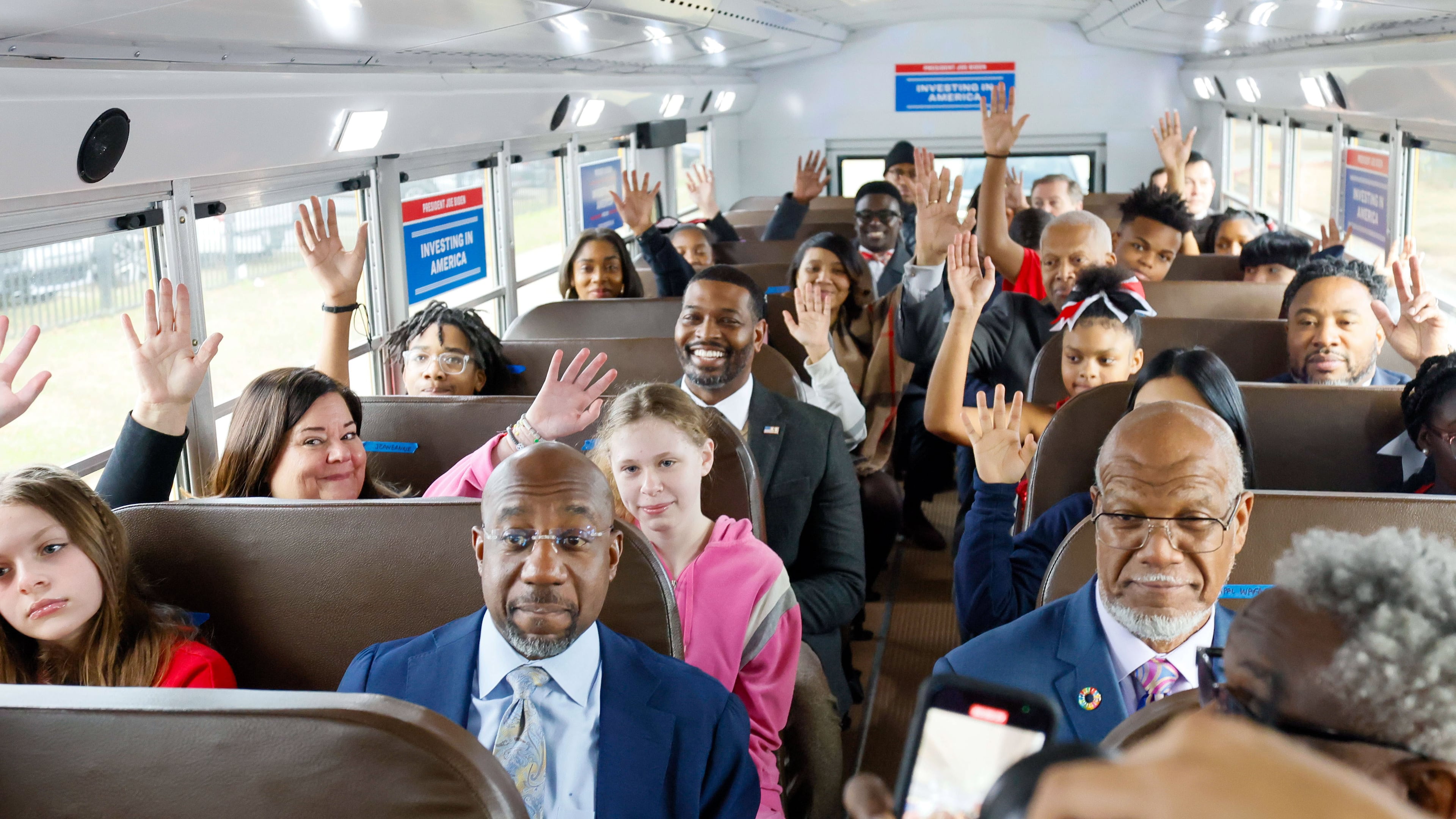 U.S. Sen. Raphael Warnock, D-Ga., and Environmental Protection Agency Administrator Michael S. Regan (two rows behind) enjoy a test ride on an electric bus in DeKalb County on Monday, Jan. 8, 2024. The school district will receive a $20 million federal grant to buy electric buses. (Miguel Martinez /miguel.martinezjimenez@ajc.com)