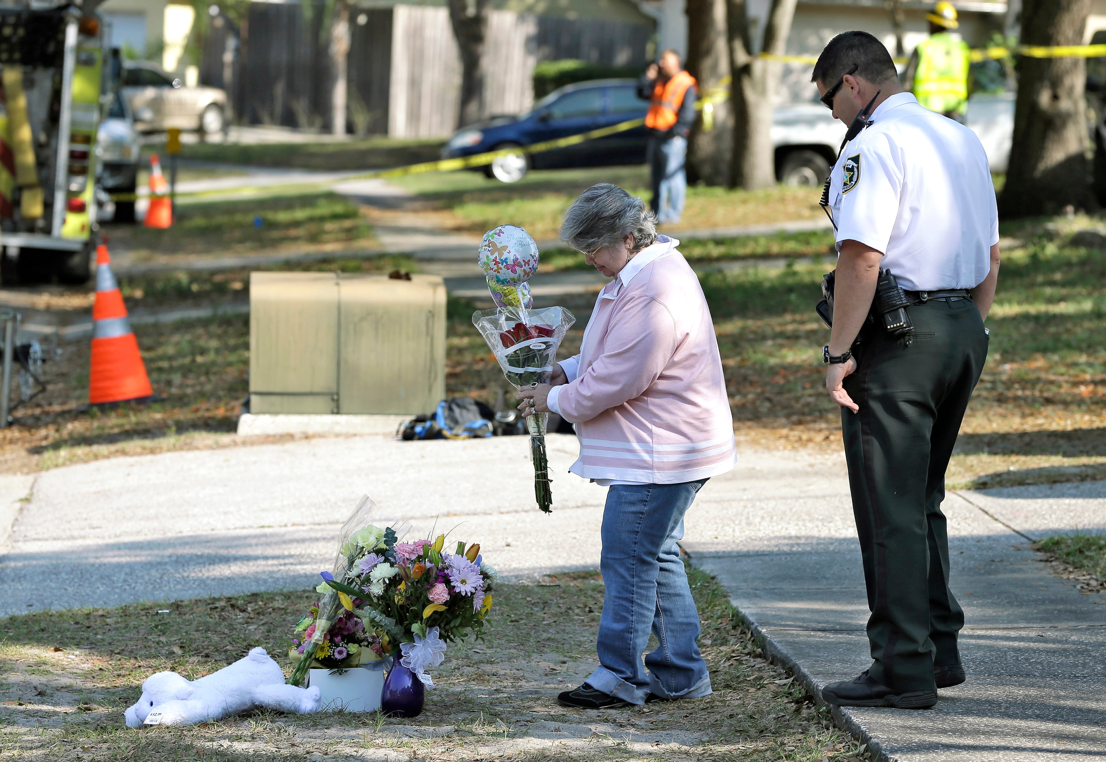 Brenda Bush is escorted by a Hillsborough County Sheriff's deputy as she places flowers at a makeshift memorial in front of the home where the sinkhole opened up.