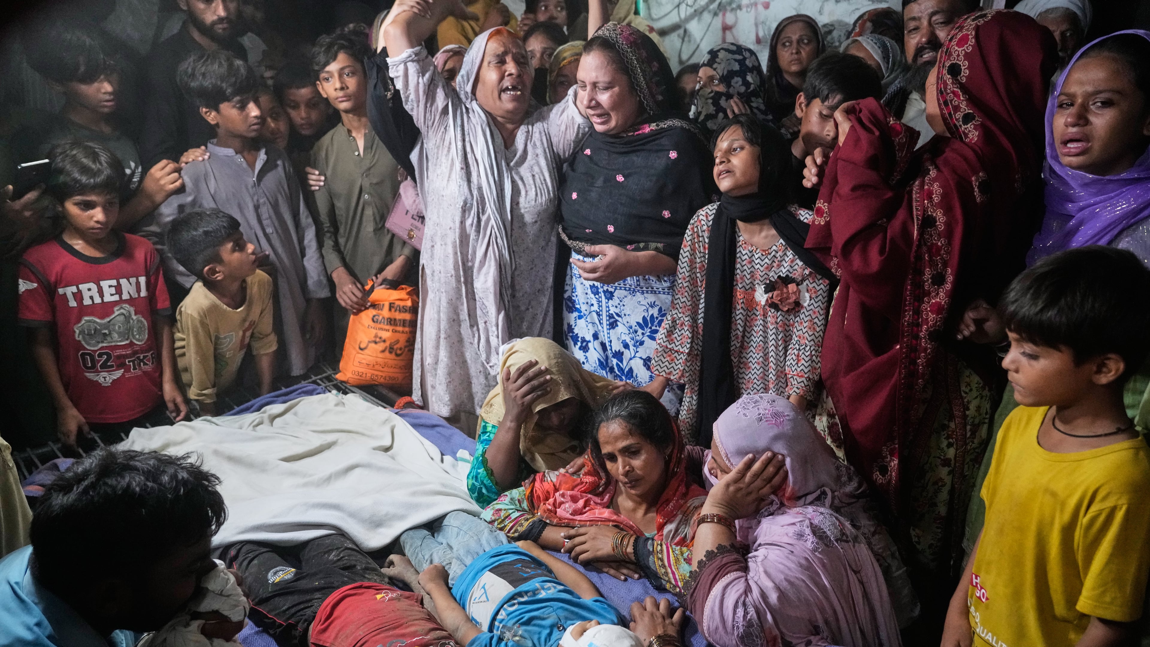 Women mourn next to the bodies of their children killed after the roof of a tutoring center under-construction collapsed, on the outskirts of Lahore, Pakistan, Tuesday, June 30, 2026. (AP Photo/K.M Chaudary)