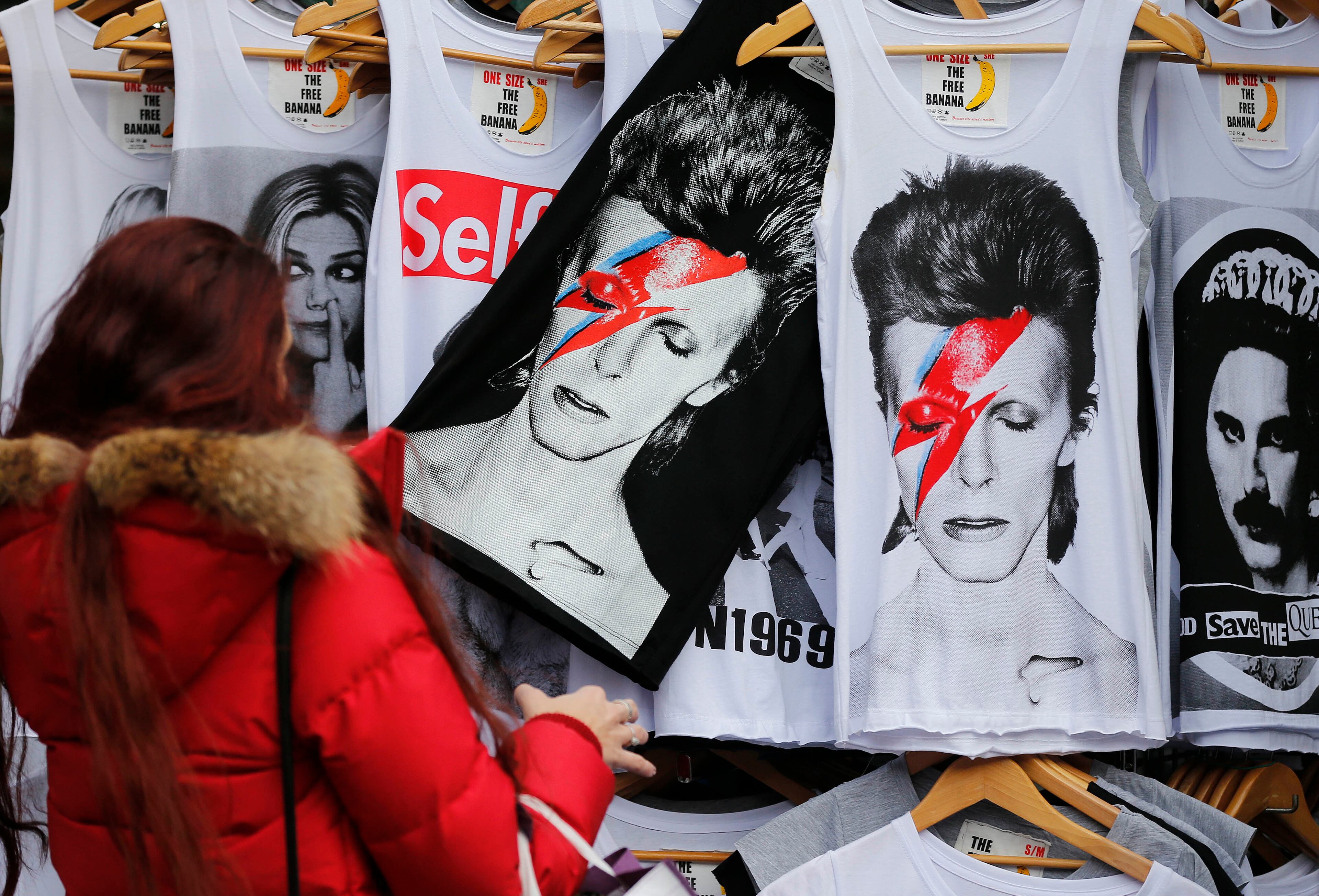A woman looks at shirts with a portrait of David Bowie, in London, Monday, Jan. 11, 2016. David Bowie, the other-worldly musician who broke pop and rock boundaries with creative musicianship, nonconformity, striking visuals and a genre-bending persona and christened Ziggy Stardust, died of cancer Sunday. He was 69 and had just released a new album.(AP Photo/Frank Augstein)