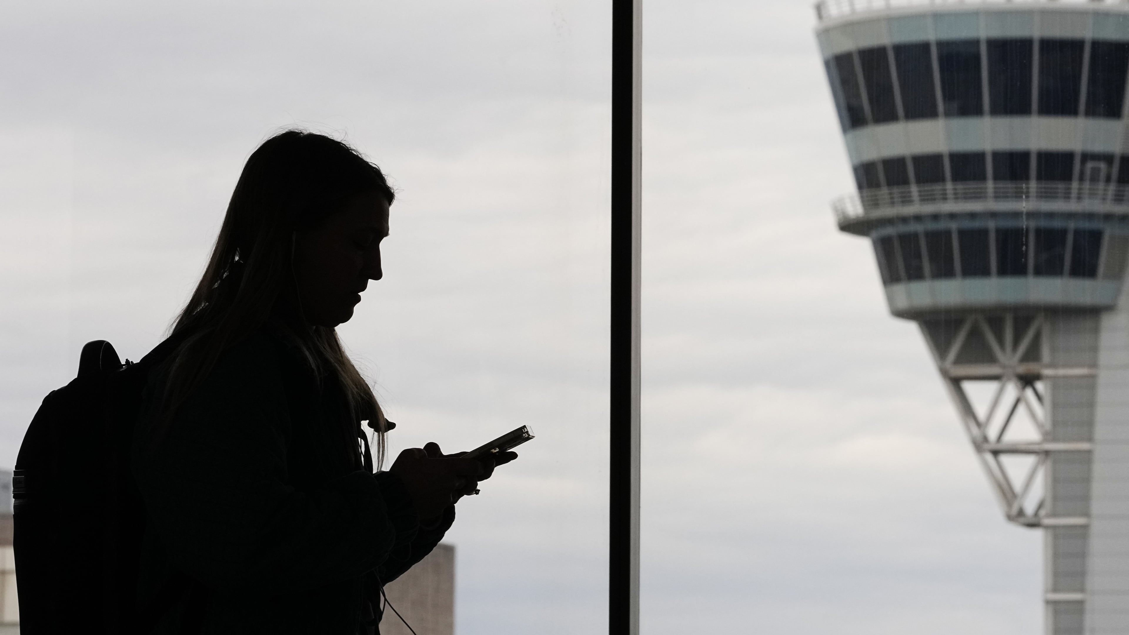 FILE - A traveler with a smartphone walks past an air traffic control tower at Philadelphia International Airport in Philadelphia on March 27, 2026. (AP Photo/Matt Rourke, File)