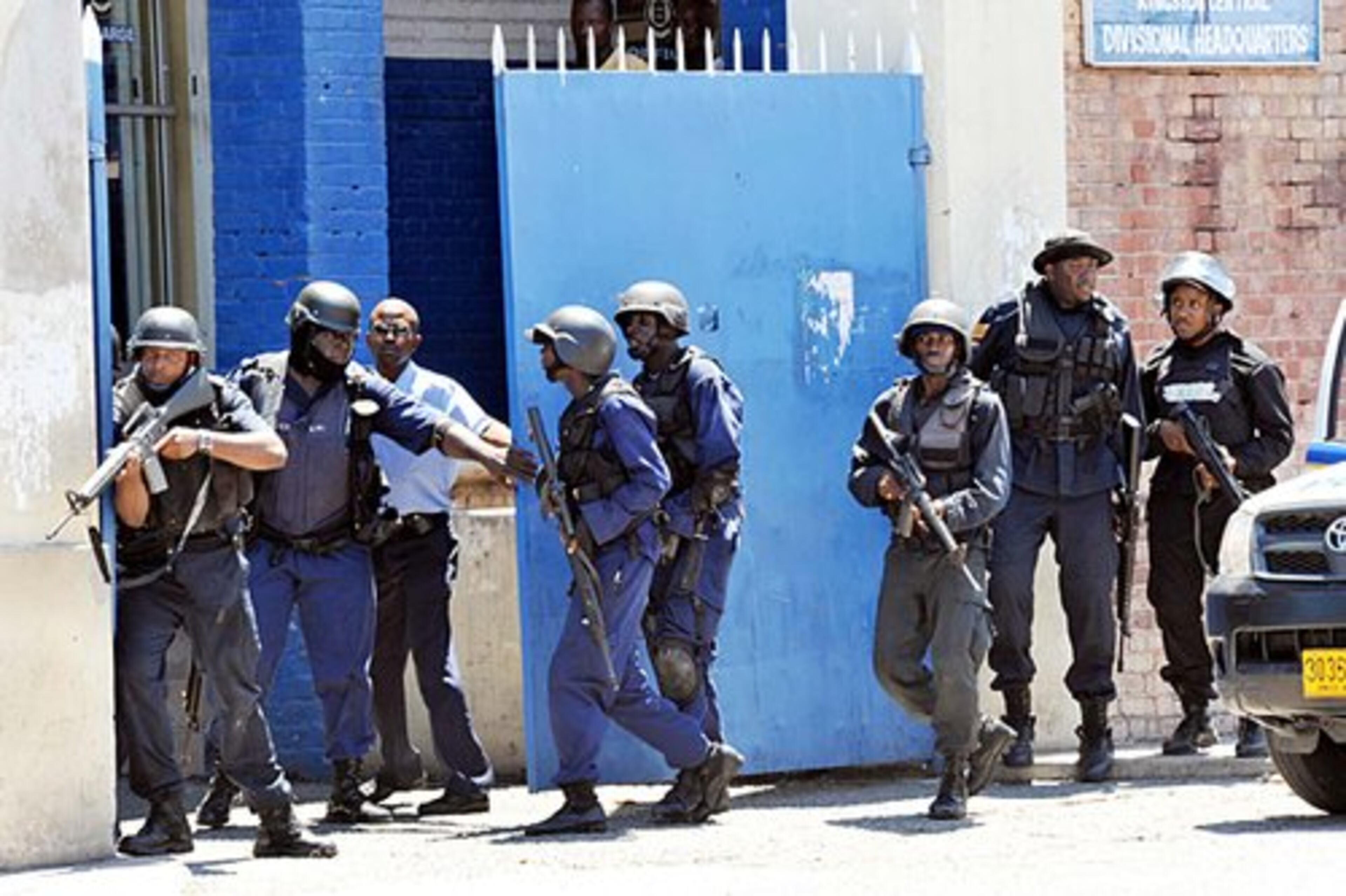 Policemen go into action at the Central Police Station gate in downtown Kingston after gunmen open fire on them.